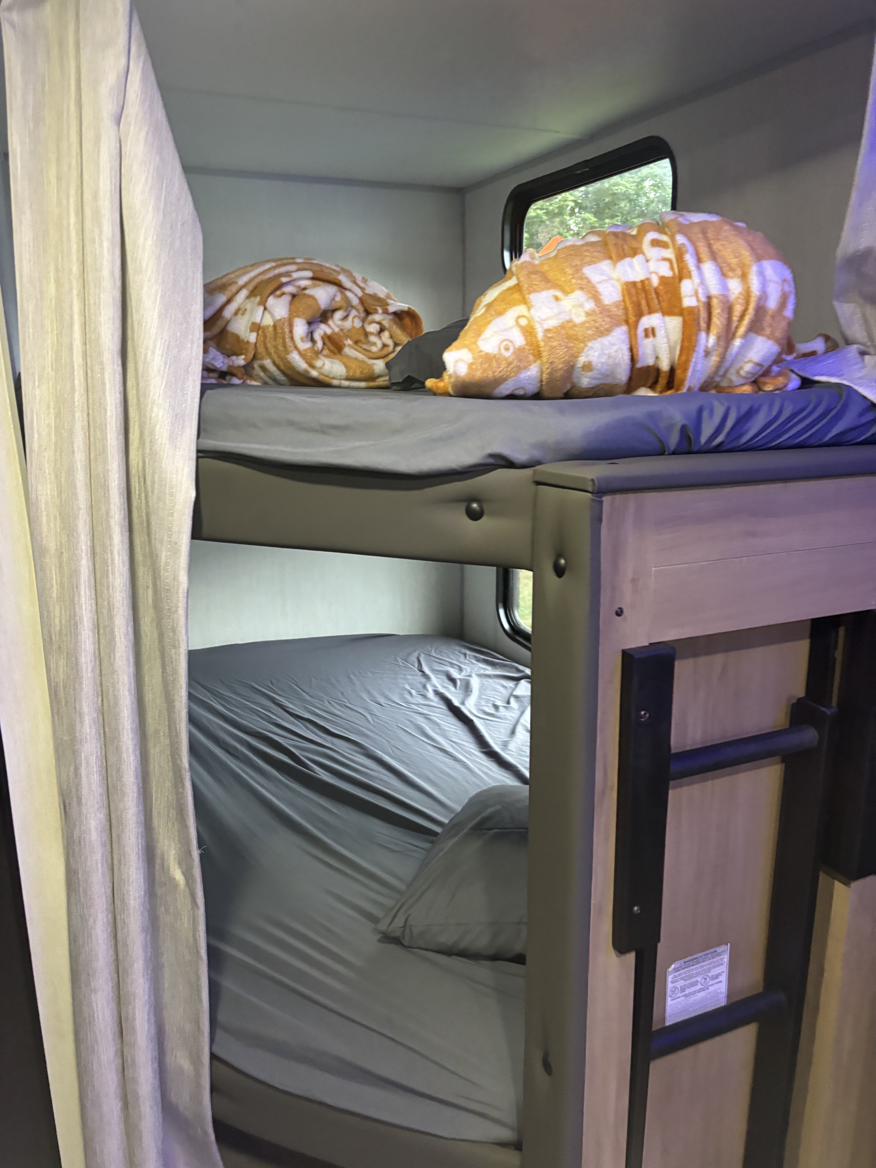 Cozy RV rental bunk beds featuring soft sheets, colorful blankets, and a window view of nature.. Forest River Cherokee 26DBH 2024