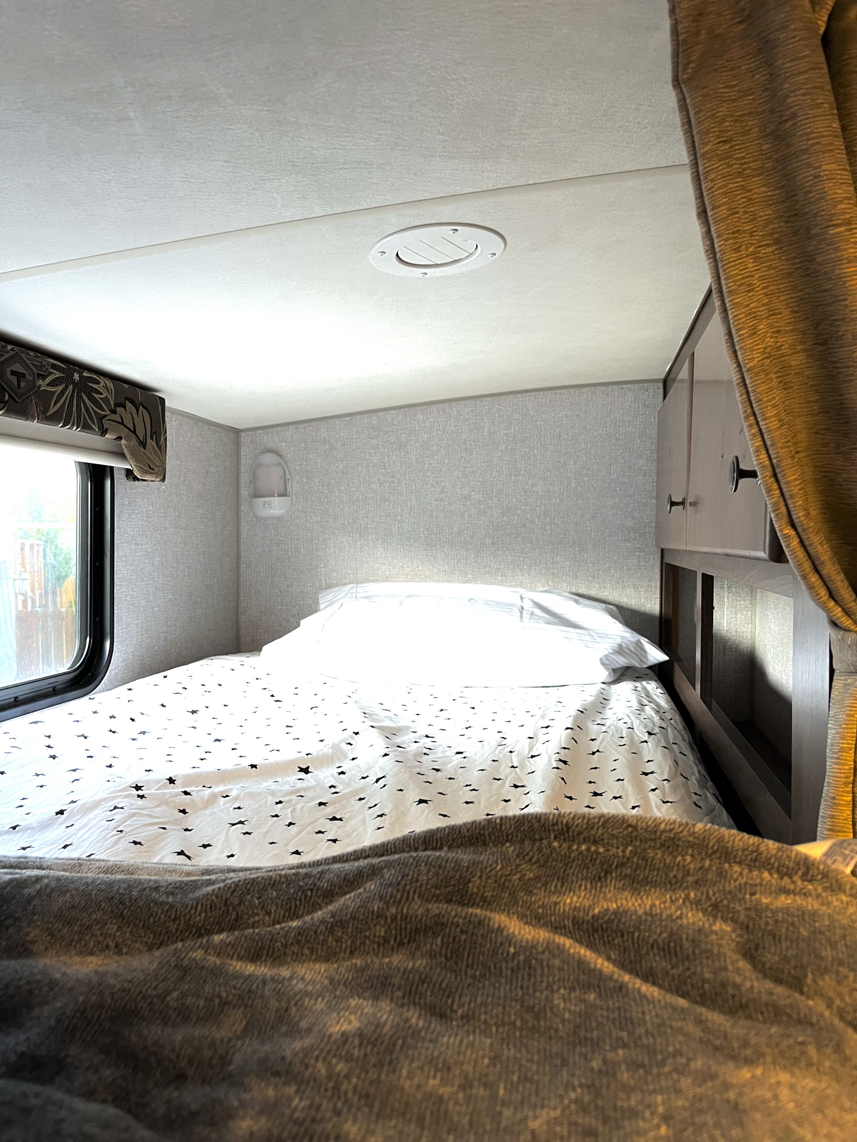 Cozy RV rental bedroom featuring a bed with star-patterned sheets, a window view, and overhead vent. Ready for your travels.. Nash Nash Trailer 2021