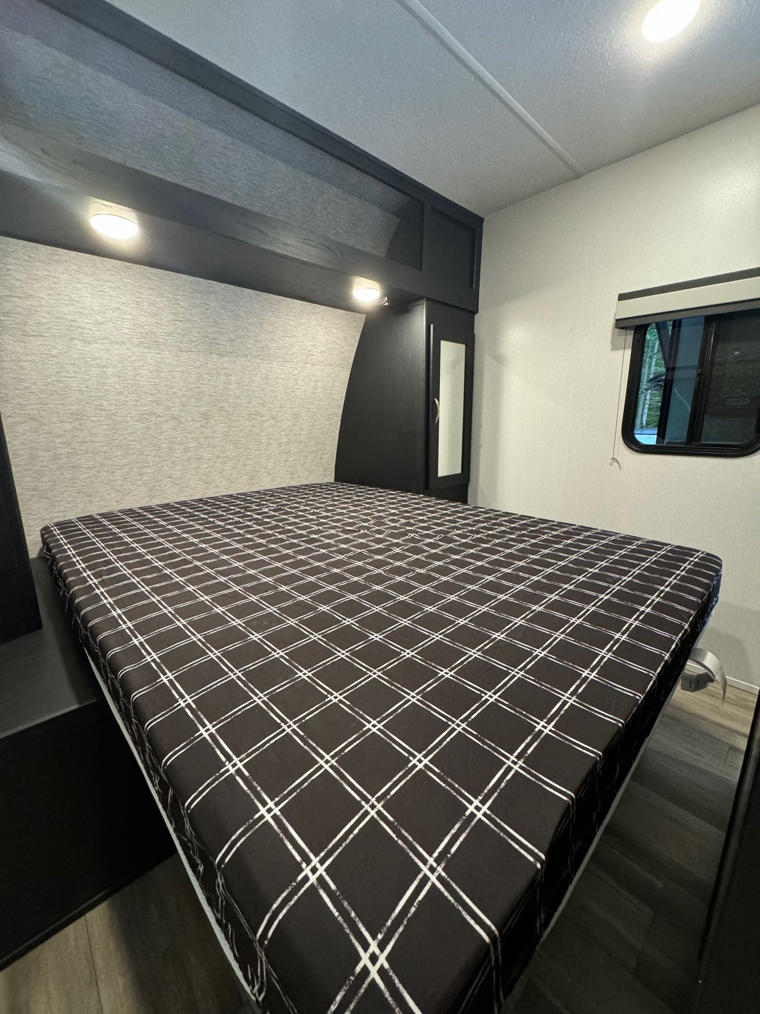 Comfortable RV rental bedroom with a plaid bed, overhead storage, and a scenic window view.. Coachmen Freedom Express 2024