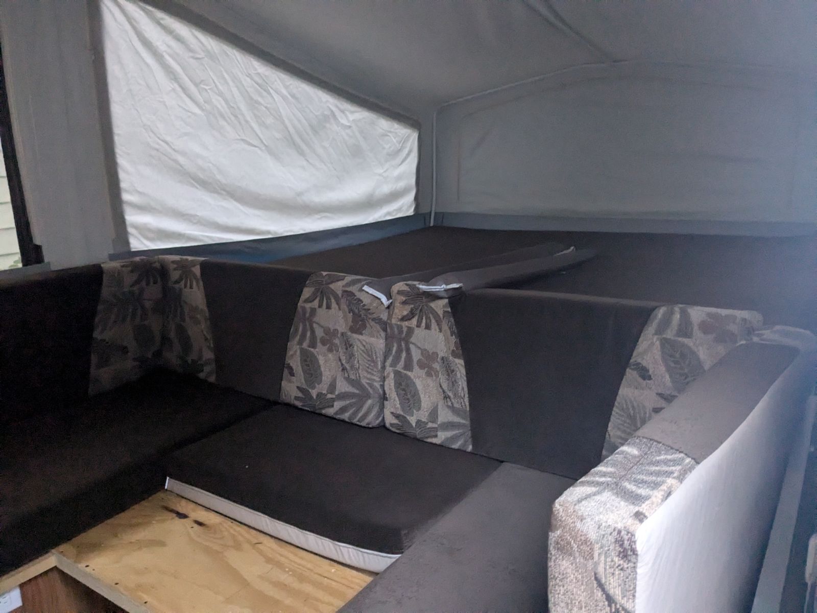 Interior of a pop-up RV rental with dark cushions & patterned backrests, showing a sleeping area and seating.. Jayco Jay 2010