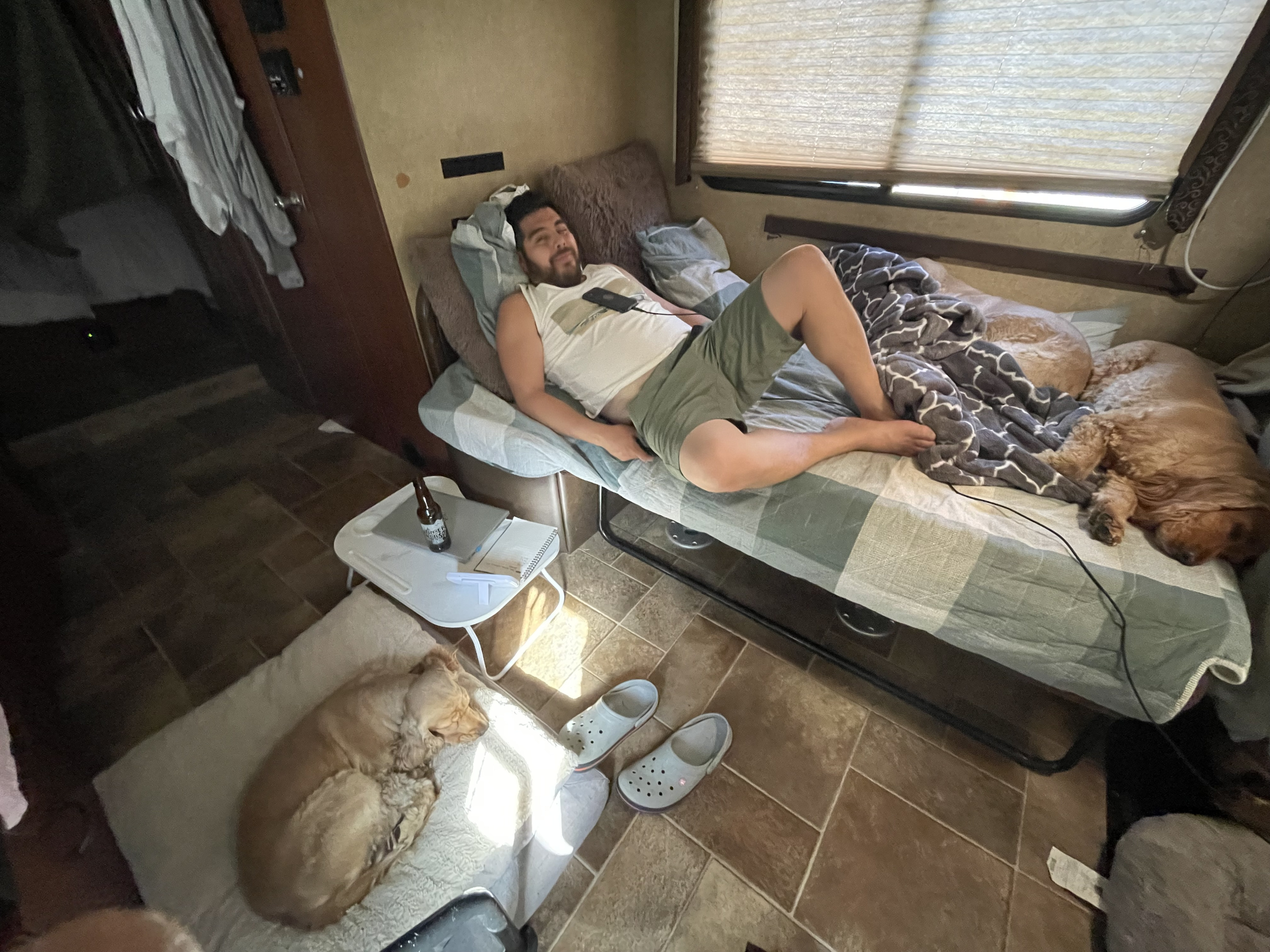 Pet-friendly RV rental setup: Man relaxing on bed, two cozy dogs, and a laptop with a beer.. Thor Four Winds 2015