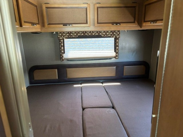 RV rental bedroom with modular bed cushions, padded headboard, window, and overhead cabinets.. Thor Axis 2016