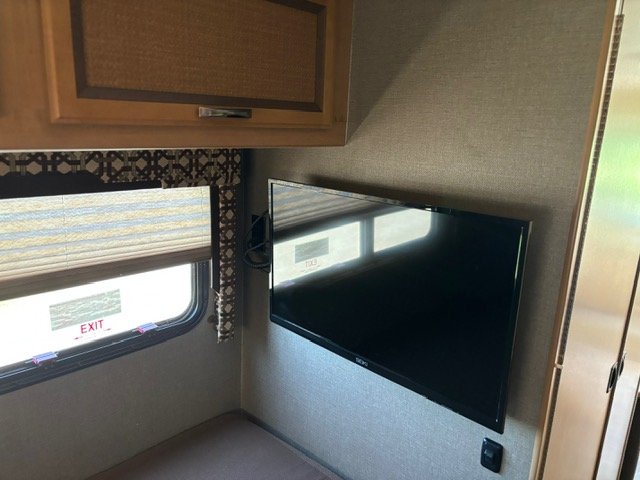 Inside an RV rental: Enjoy entertainment with a wall-mounted TV, privacy with window blinds, and storage in wood cabinets.. Thor Axis 2016