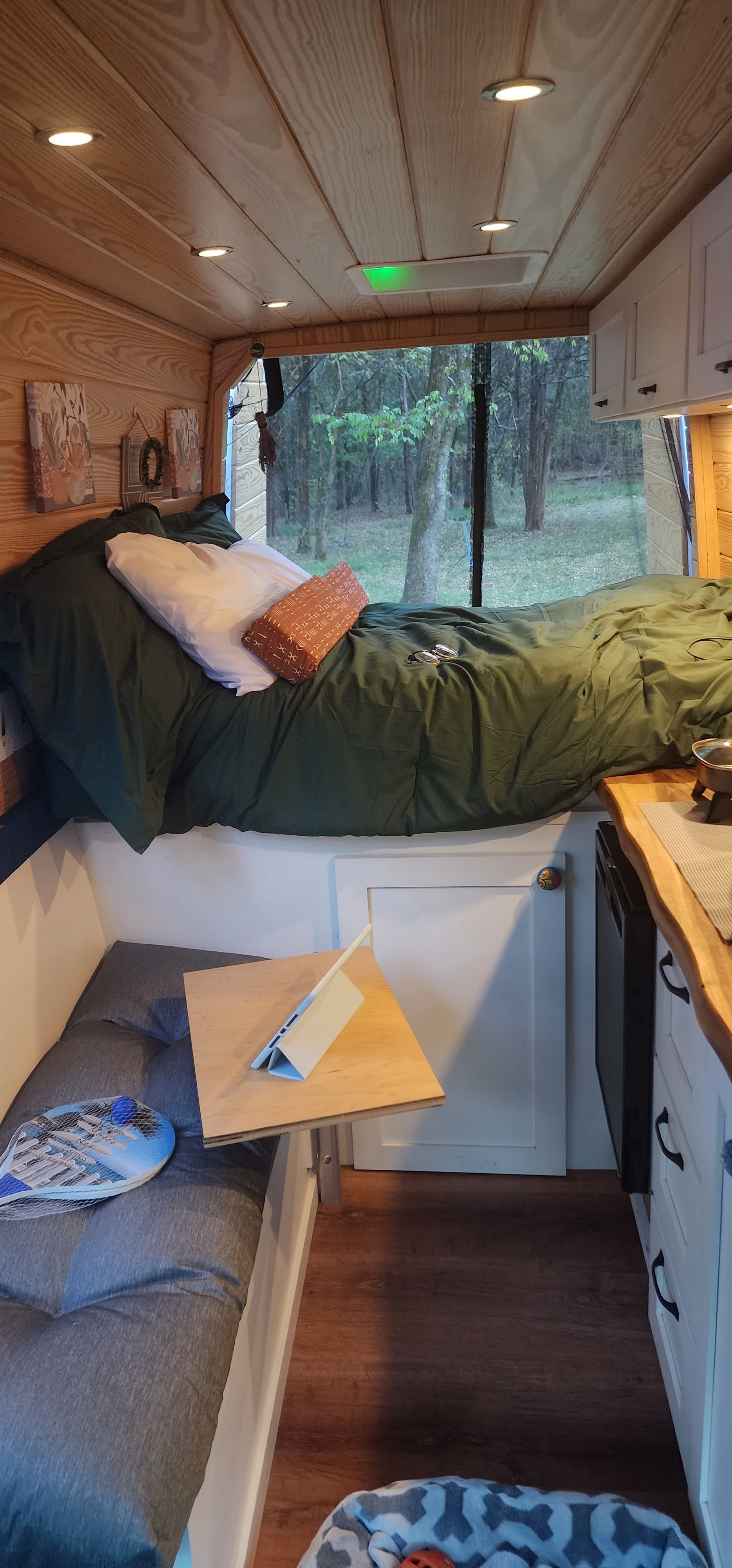 This RV rental interior features a cozy bed with forest views, a compact kitchen, and a workspace with a tablet.. Mercedes Sprinter 1500 2020