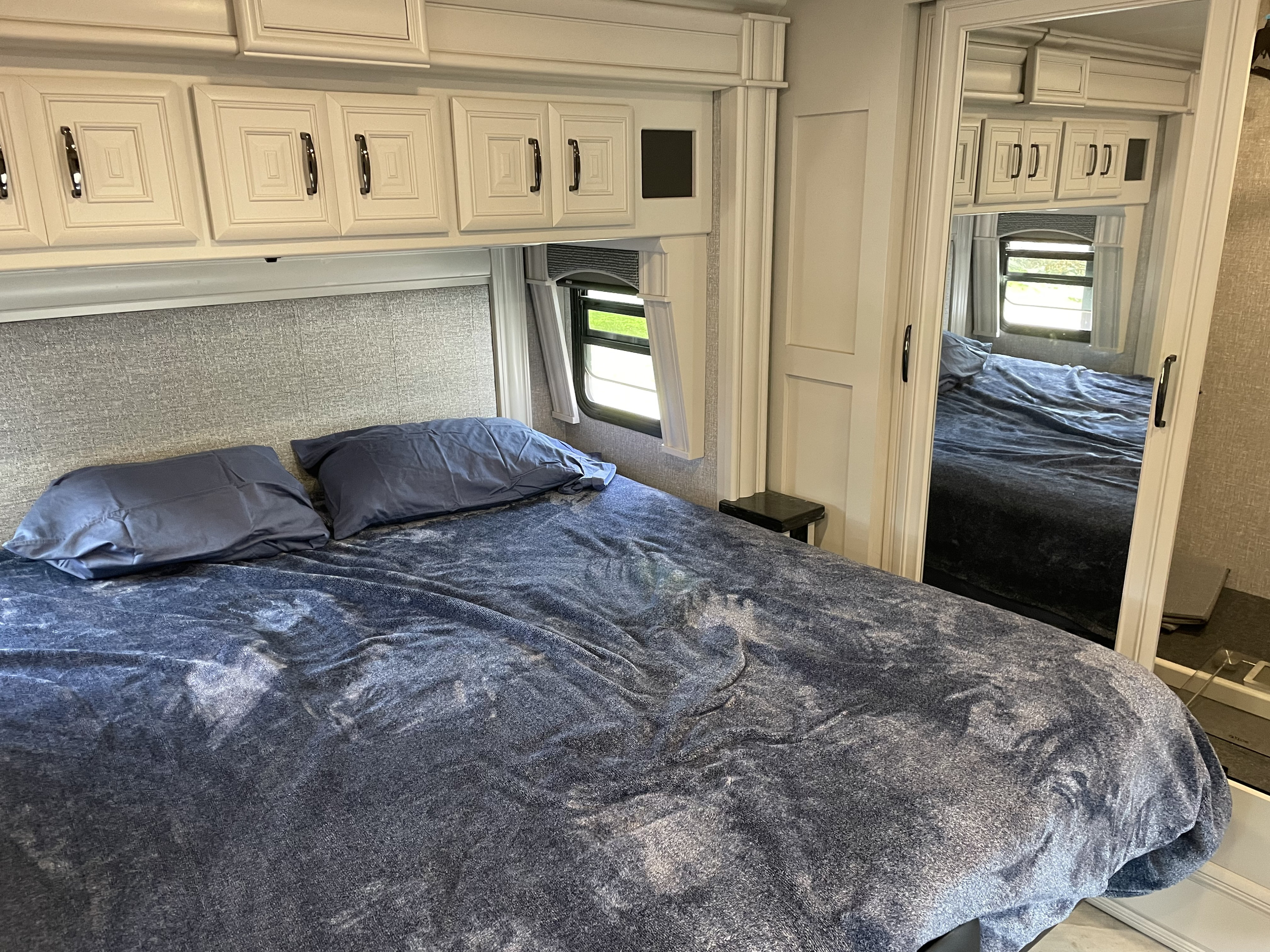 Spacious RV rental bedroom with comfy bed, overhead cabinets, window, and full-length mirror.. Fleetwood Discovery LXE 2021