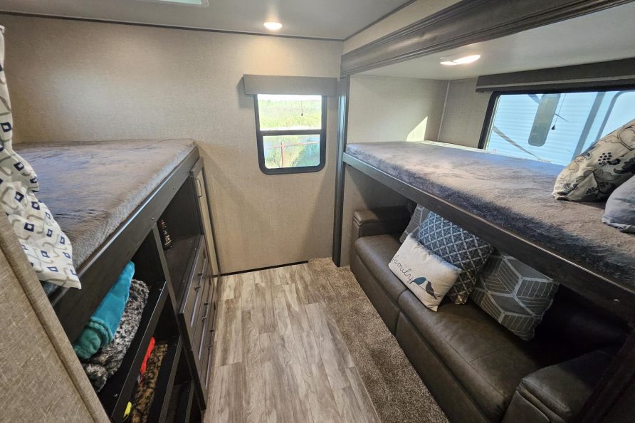 RV rental interior showing bunk beds, one with storage, another over a sofa. Cozy travel space.. Grand Design Reflection 2022