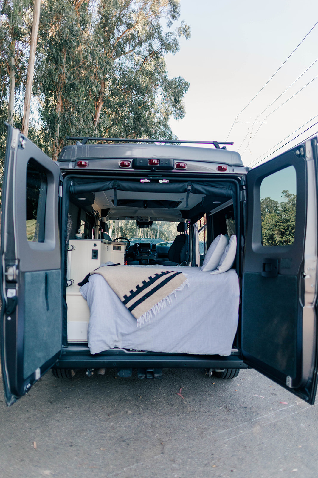 Inside a grey rv rental camper van: open rear doors reveal a cozy bed, cushions, and built-in amenities. Ready for adventure.. Pleasure-Way Pleasure-Way Class B 2022