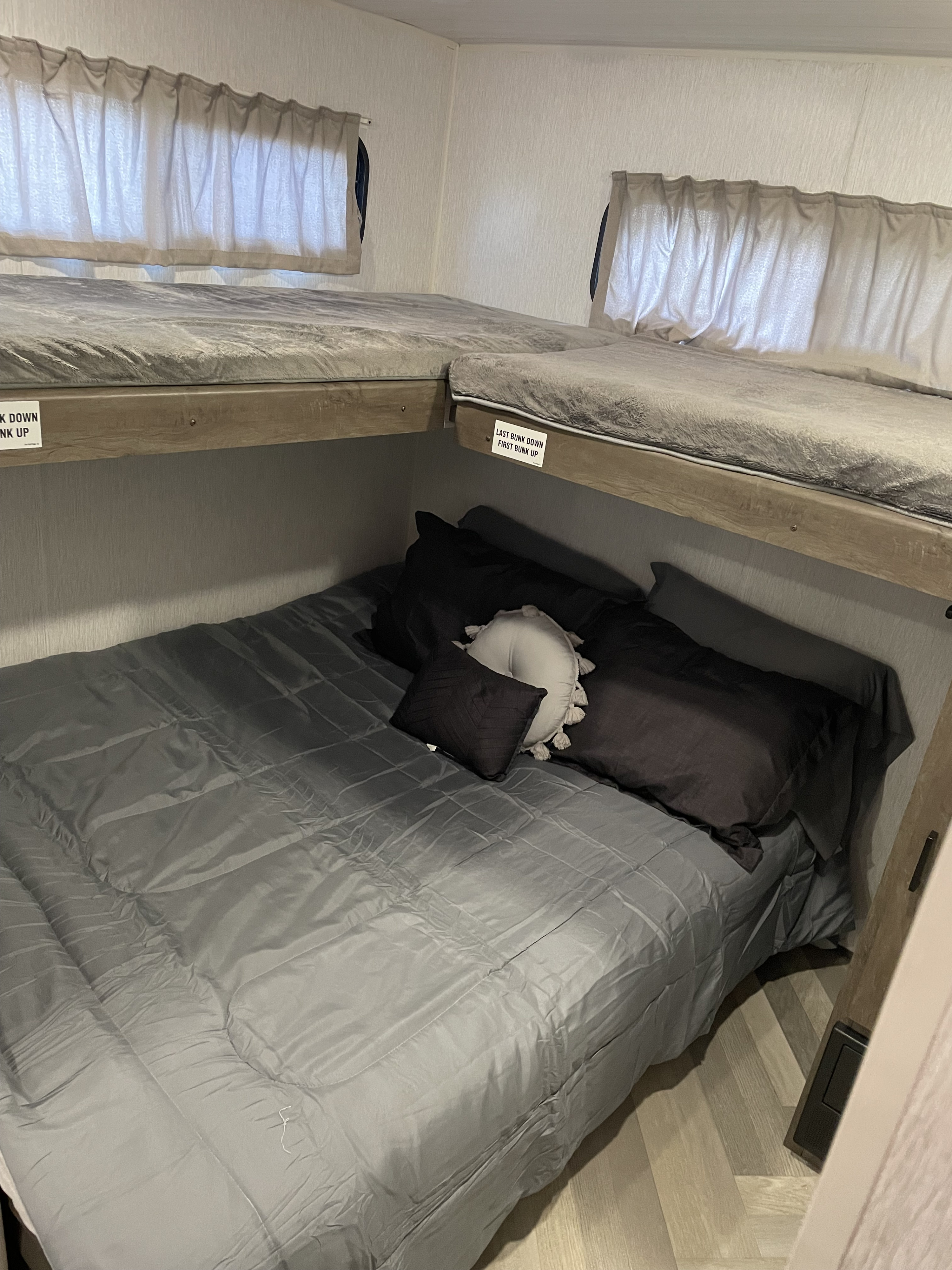 This RV rental offers triple bunk beds: a spacious lower bed and two upper bunks, perfect for families. Grey bedding shown.. Forest River Wildwood 2022