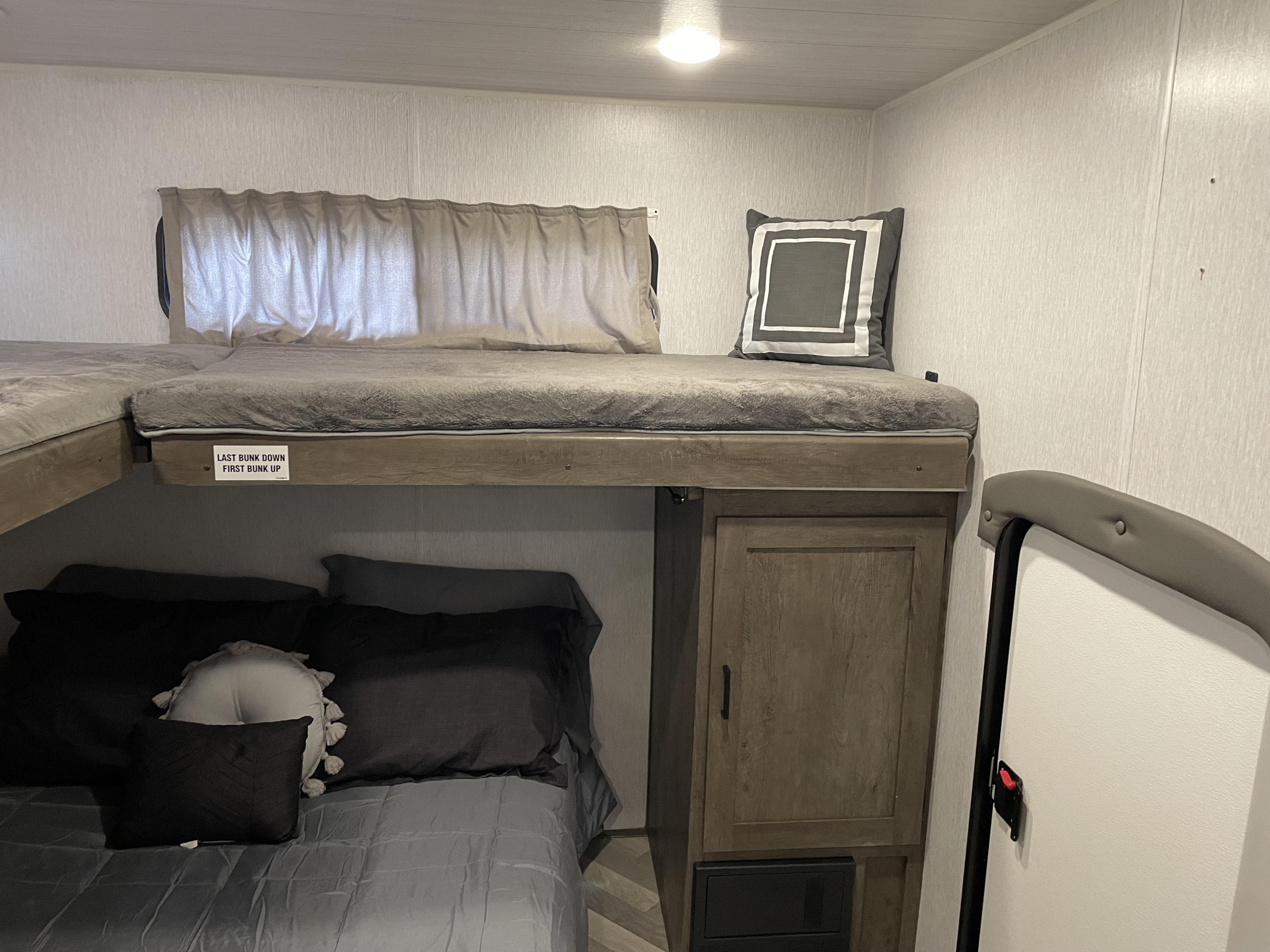 This RV rental features stacked bunk beds, offering compact sleeping. The upper bunk has a window; a sign indicates operation: 'LAST BUNK DOWN FIRST BUNK UP'.. Forest River Wildwood 2022