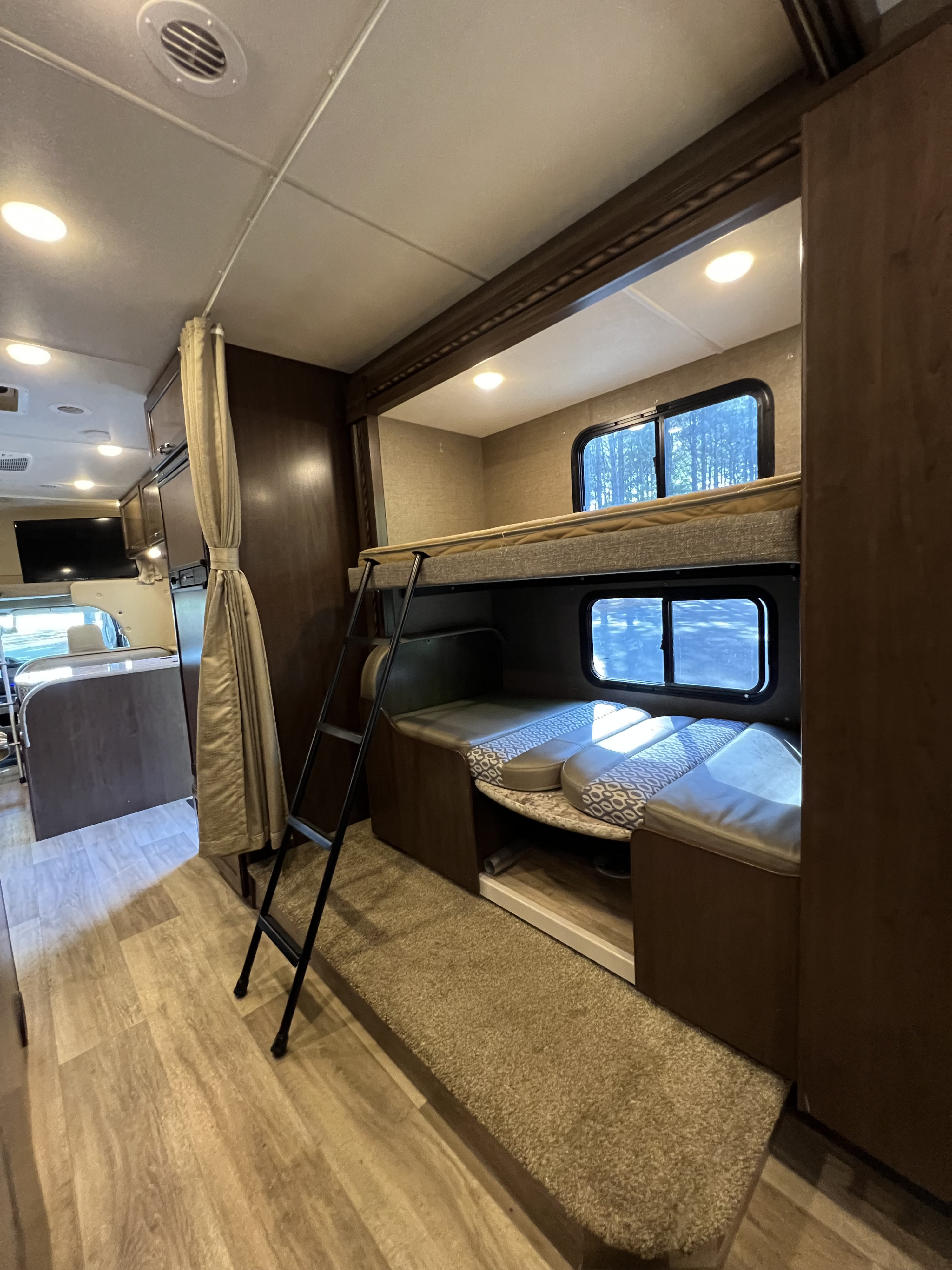 RV rental interior: cozy bunk beds with ladder, lower seating, windows, and light wood flooring for comfortable travel.. Thor Freedom Elite 2018