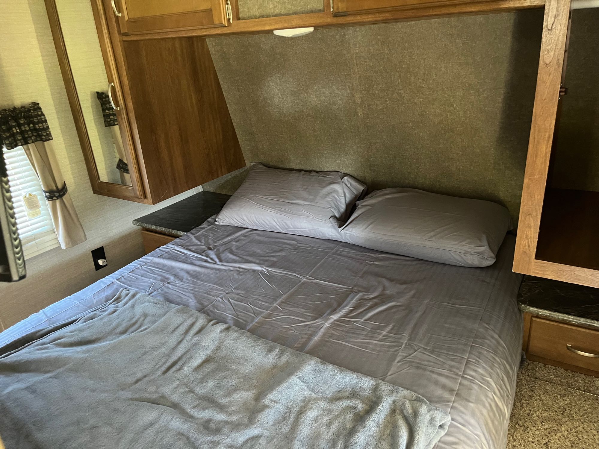 RV rental bedroom: A comfortable bed with gray linens, surrounded by wooden storage cabinets and a window, ideal for travel.. Keystone RV Springdale 2017