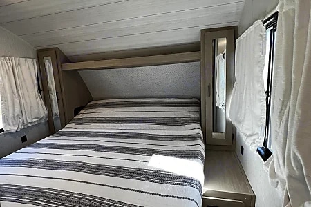 Cozy RV rental bedroom featuring a striped bed, overhead shelf, and compact mirrored storage. Great for road trips!. Forest River Salem Cruise Lite 2024