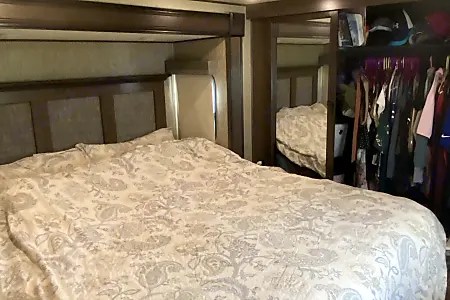 Step into comfort with this cozy RV rental bedroom, featuring a large patterned bed and mirrored closet, perfect for your travels.. Grand Design Solitude 2019