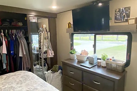 Cozy bedroom in an RV rental, featuring a closet, dresser, TV, and window view of the outdoors. Great for travel!. Grand Design Solitude 2019