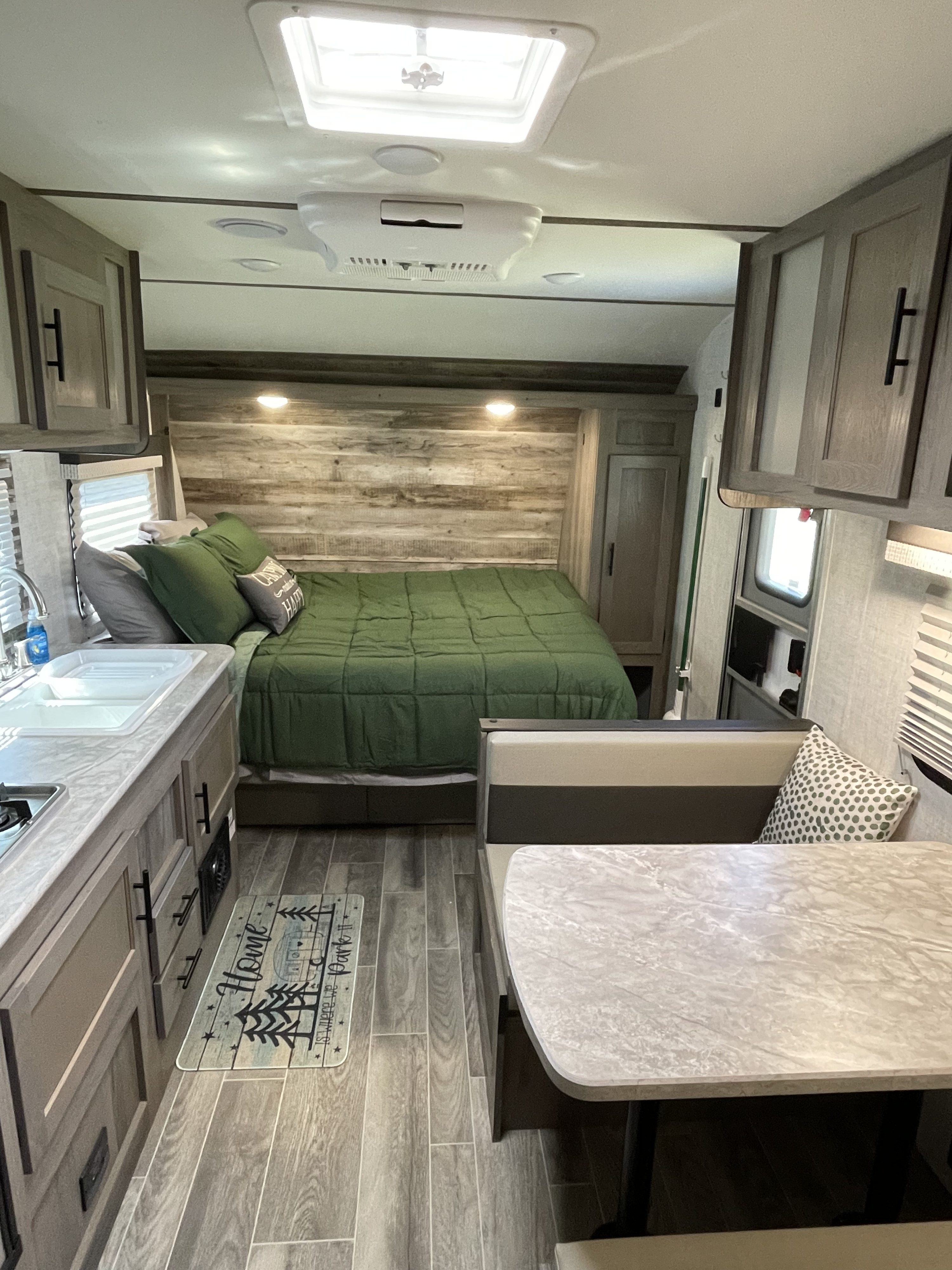 Bright RV rental interior with a large bed, kitchen sink, and dinette. Grey wood-look floors, modern cabinetry.. Gulf Stream Ameri-Lite Super Lite 2021