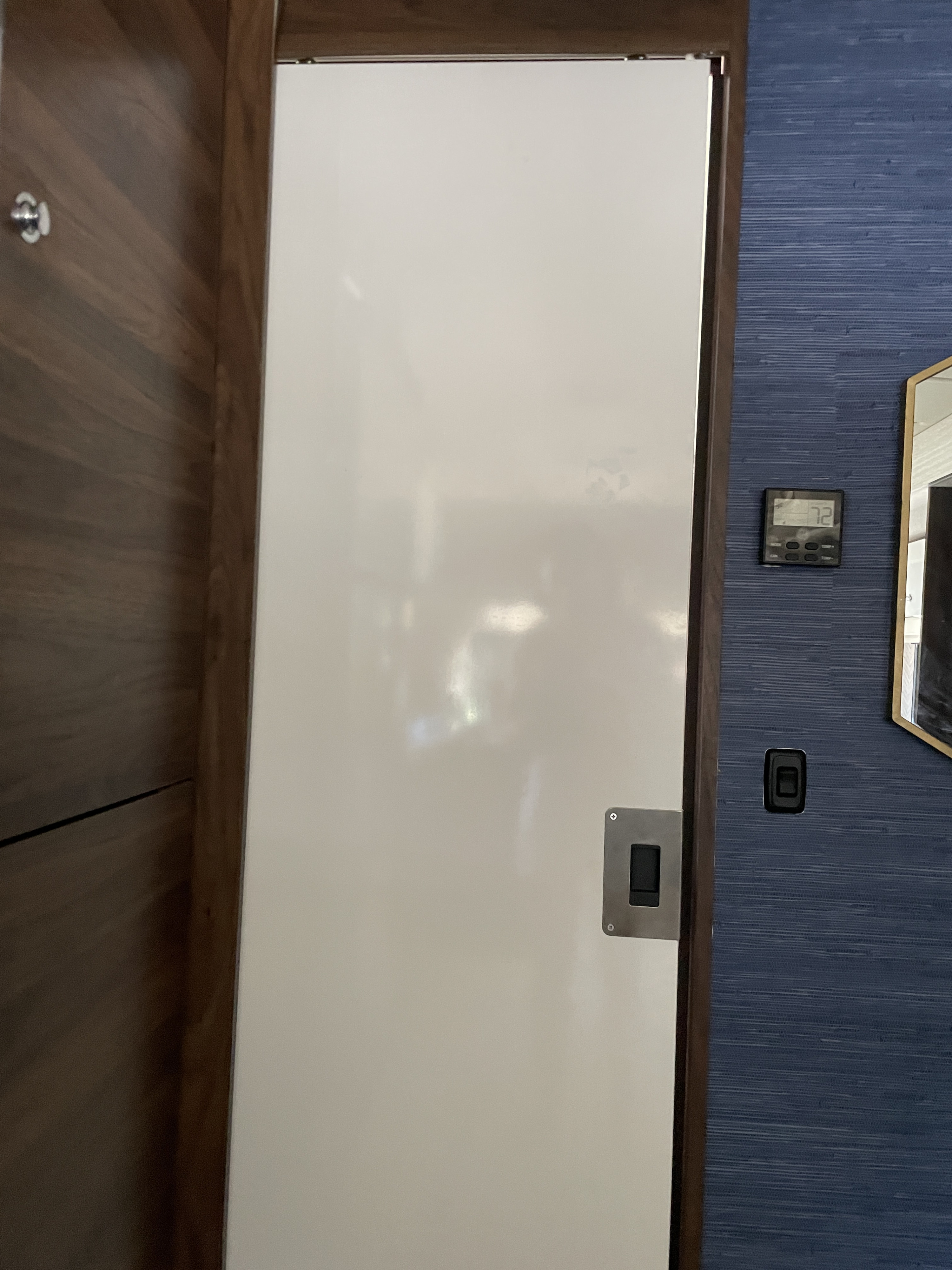 Modern RV rental interior: A white door, dark wood paneling, blue textured wall, and thermostat displaying 72 degrees.. Winnebago View 2021