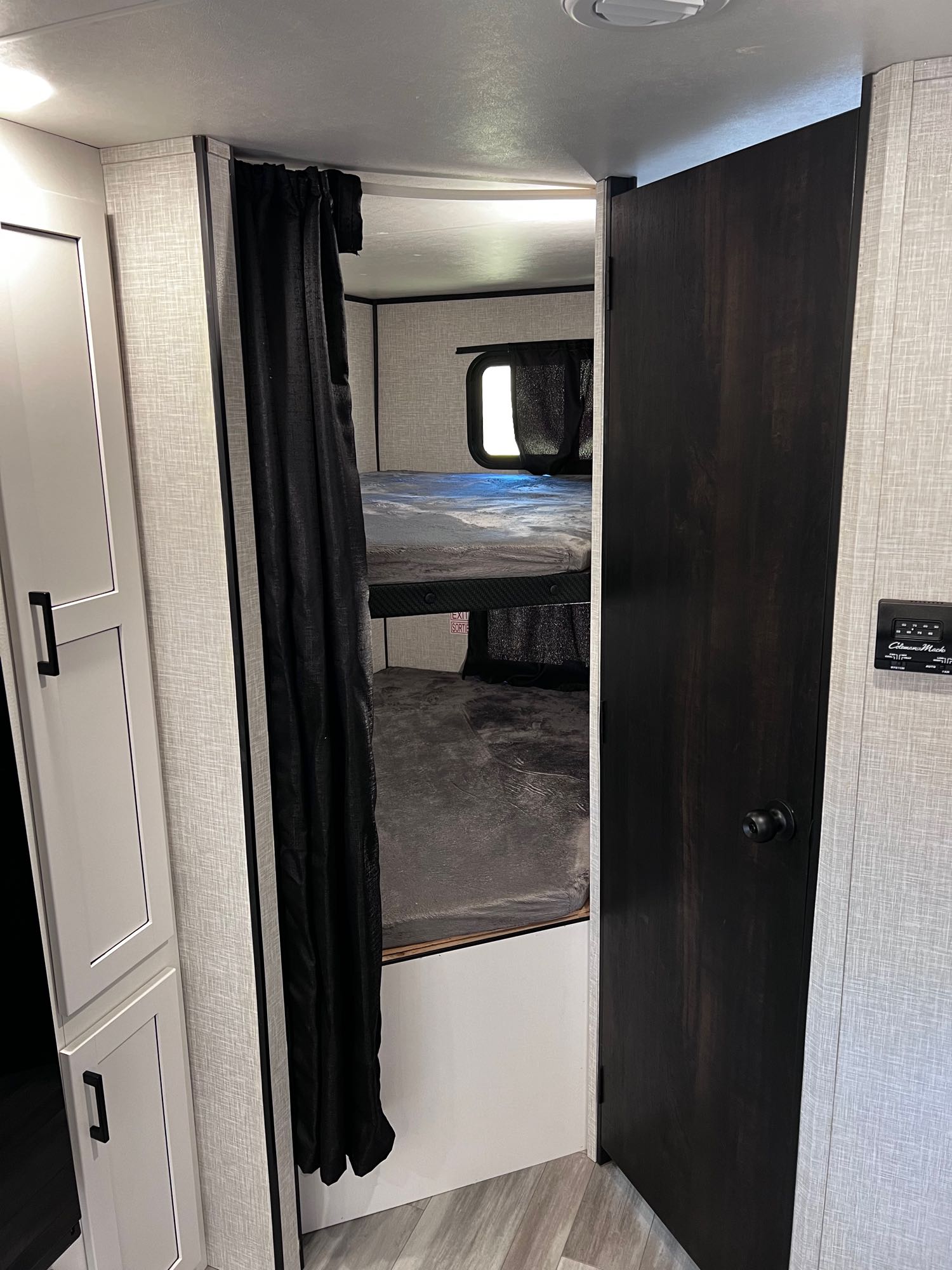 Cozy bunk beds in an RV rental, covered by a dark curtain, next to a dark wooden door and light-textured walls.. Highland Ridge RV Open Range 2024