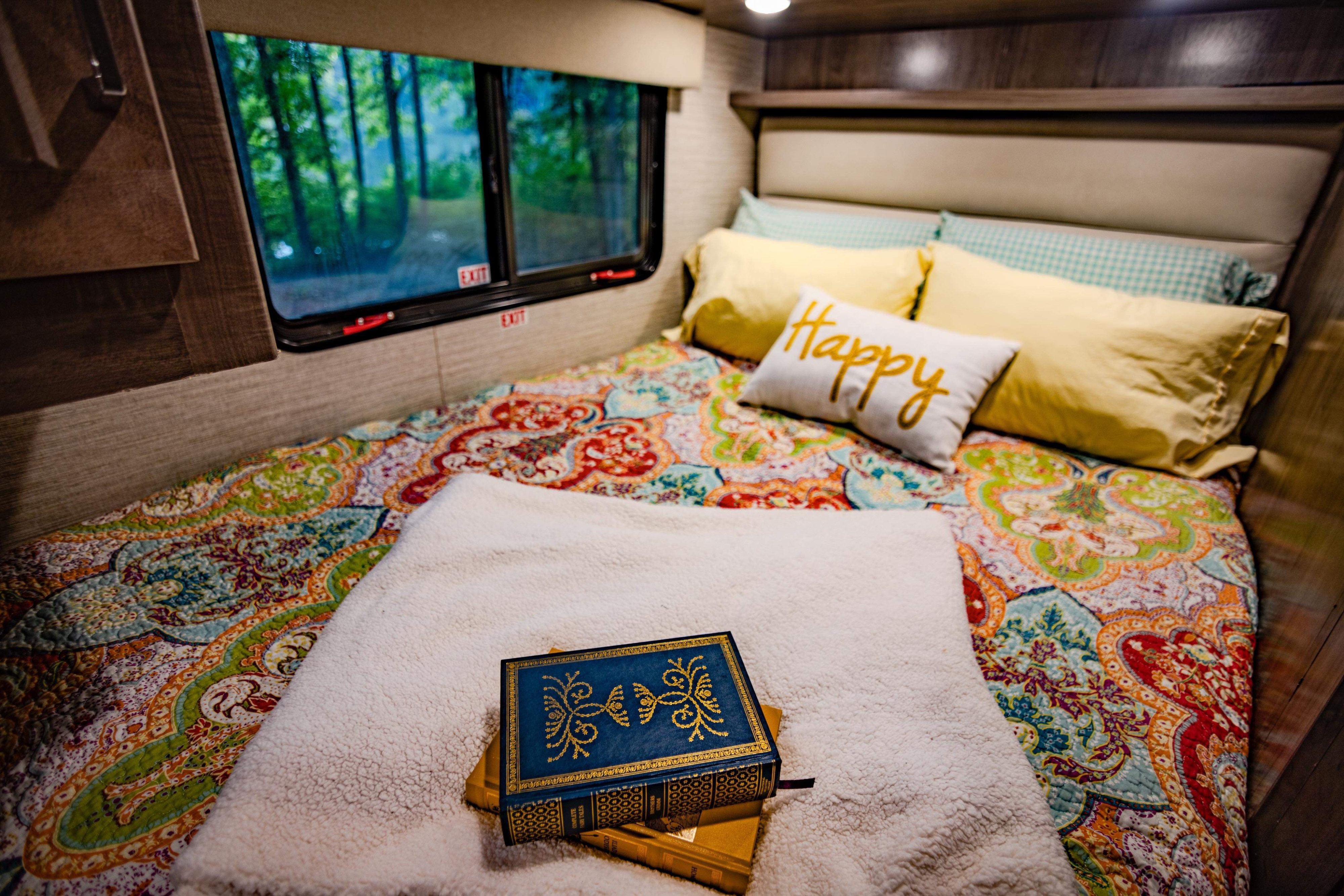 Escape to nature in a cozy RV rental bedroom, complete with colorful bedding, books, and forest views through the window.. Winnebago Minnie Winnie 2021