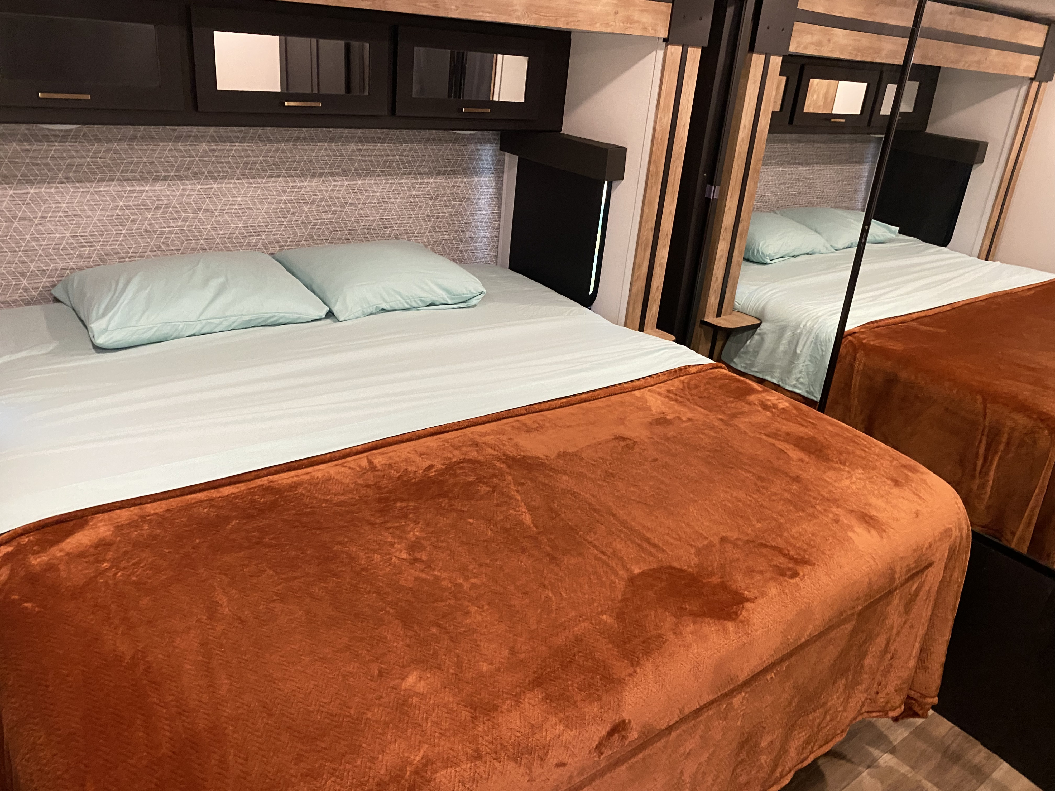 Comfortable RV rental bedroom with a light blue bed, soft rust blanket, and modern dark wood cabinets with mirrored fronts.. Keystone RV Outback 2022