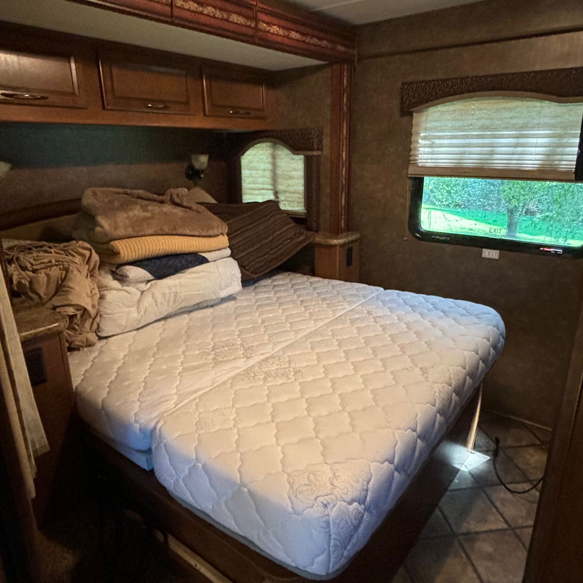 Inside an RV rental: a compact bedroom with an inviting bed, overhead storage, and an emergency exit window.. Thor Four Winds 2014