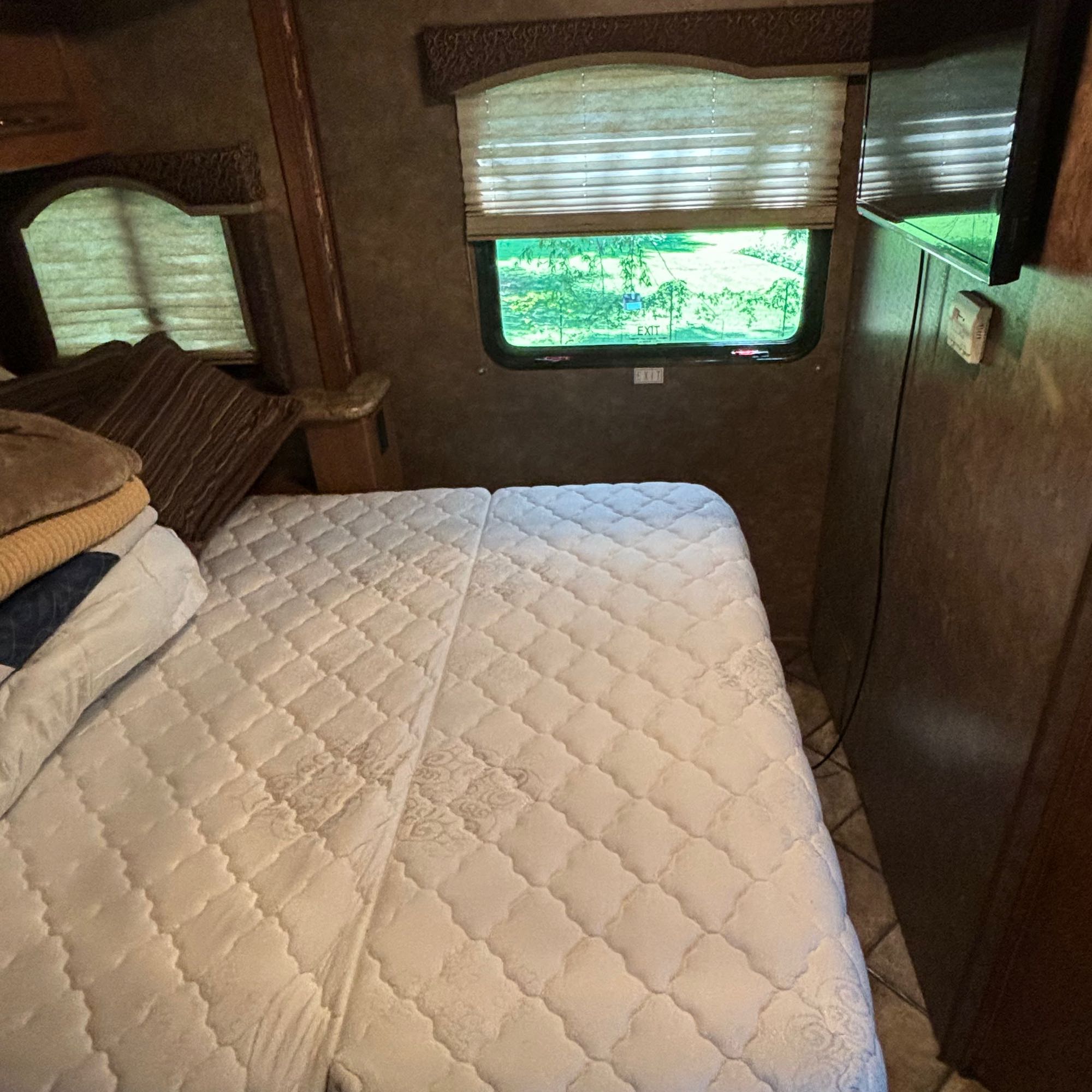 RV rental bedroom with a quilted bed, window showing green trees, and mounted TV. Ready for your next adventure.. Thor Four Winds 2014