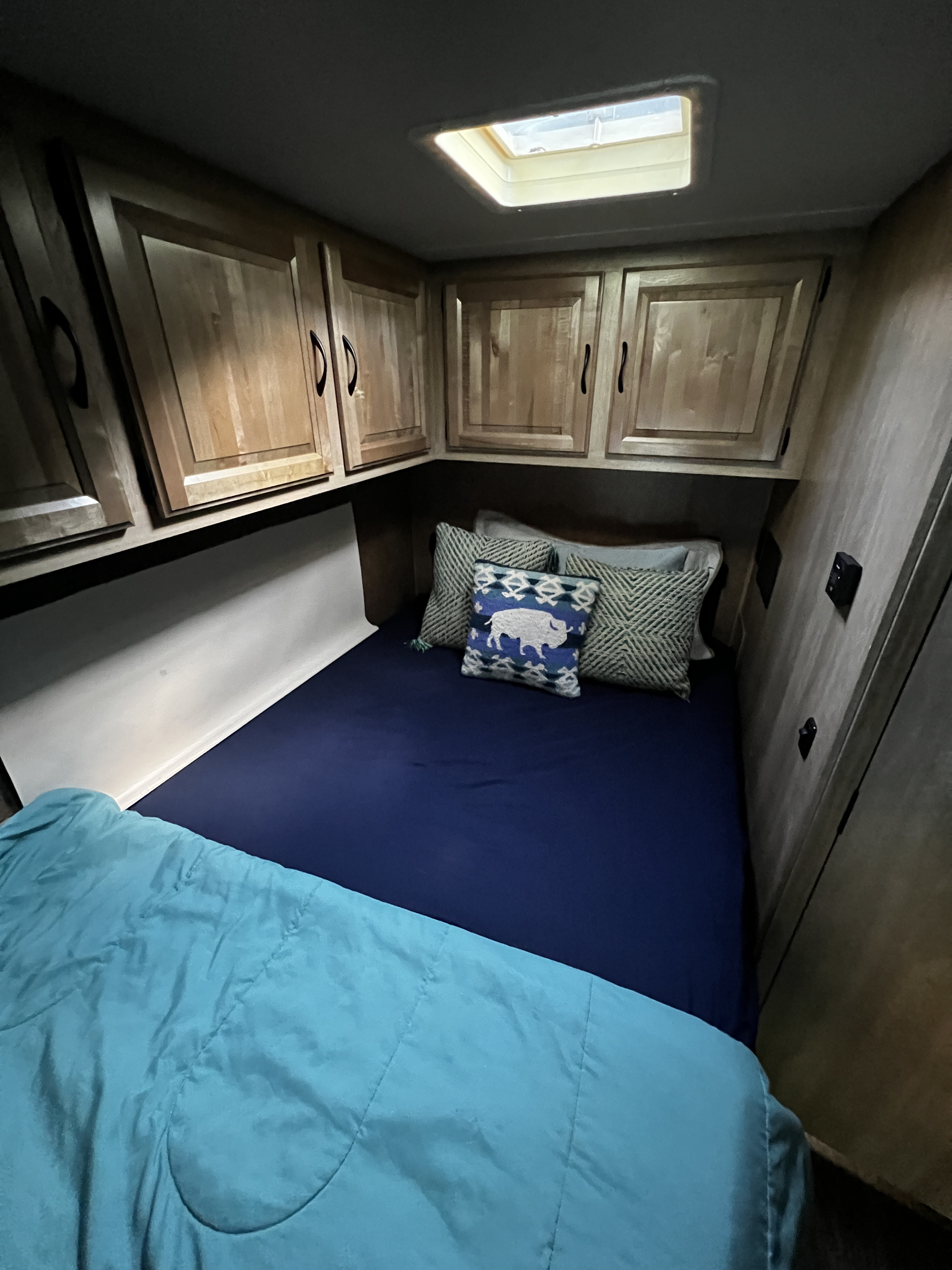Inside an RV rental, this cozy bedroom features a bed with blue bedding, overhead cabinets, and a skylight.. Forest River Coachmen Prism 2016