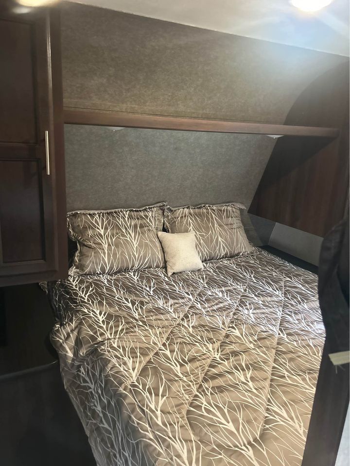 Cozy RV rental bedroom featuring a comfortable bed with unique tree-patterned bedding, overhead storage, and wood accents.. Jayco Jay Flight 2019