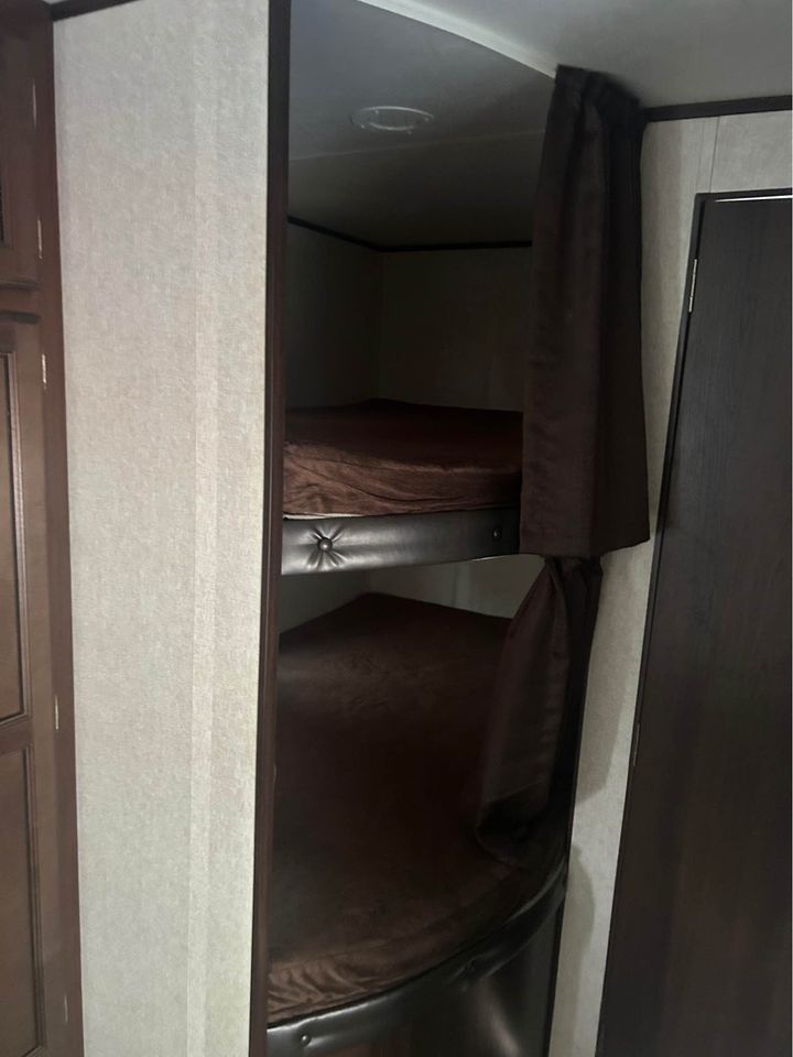 This RV rental features stacked bunk beds with dark brown mattresses and privacy curtains, ideal for compact sleeping in a travel trailer.. Jayco Jay Flight 2019