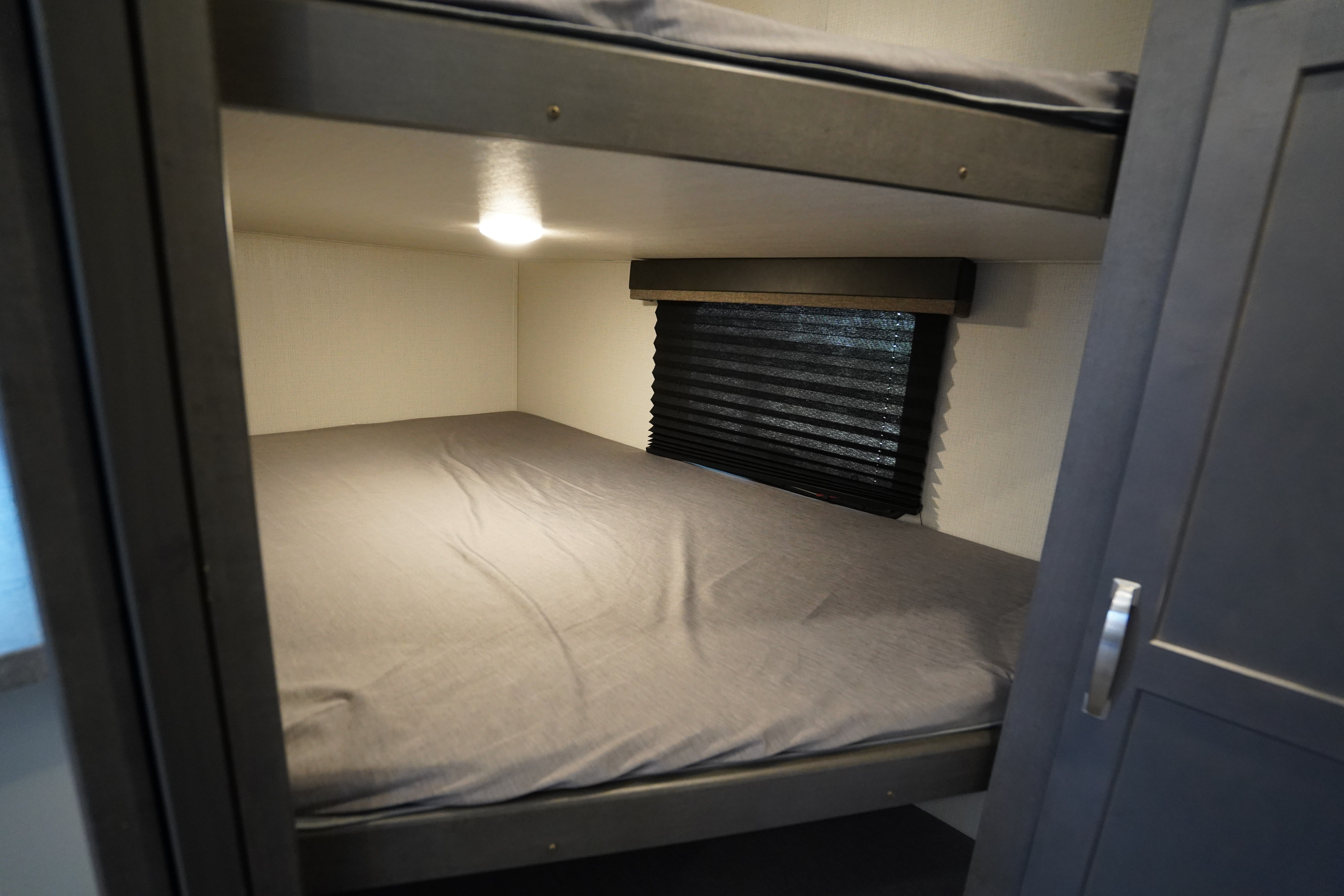Cozy RV rental bunk beds, perfect for family sleeping. Features a comfortable lower bed, window blind, and interior lighting.. Keystone Cougar 2024
