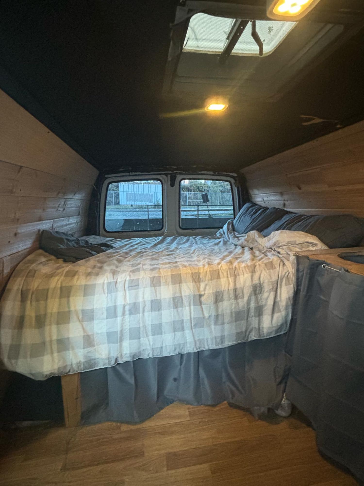 Cozy camper van bedroom with plaid bed, wooden walls, and rear windows. Perfect for your next RV rental adventure.. Gmc Savanna 1998