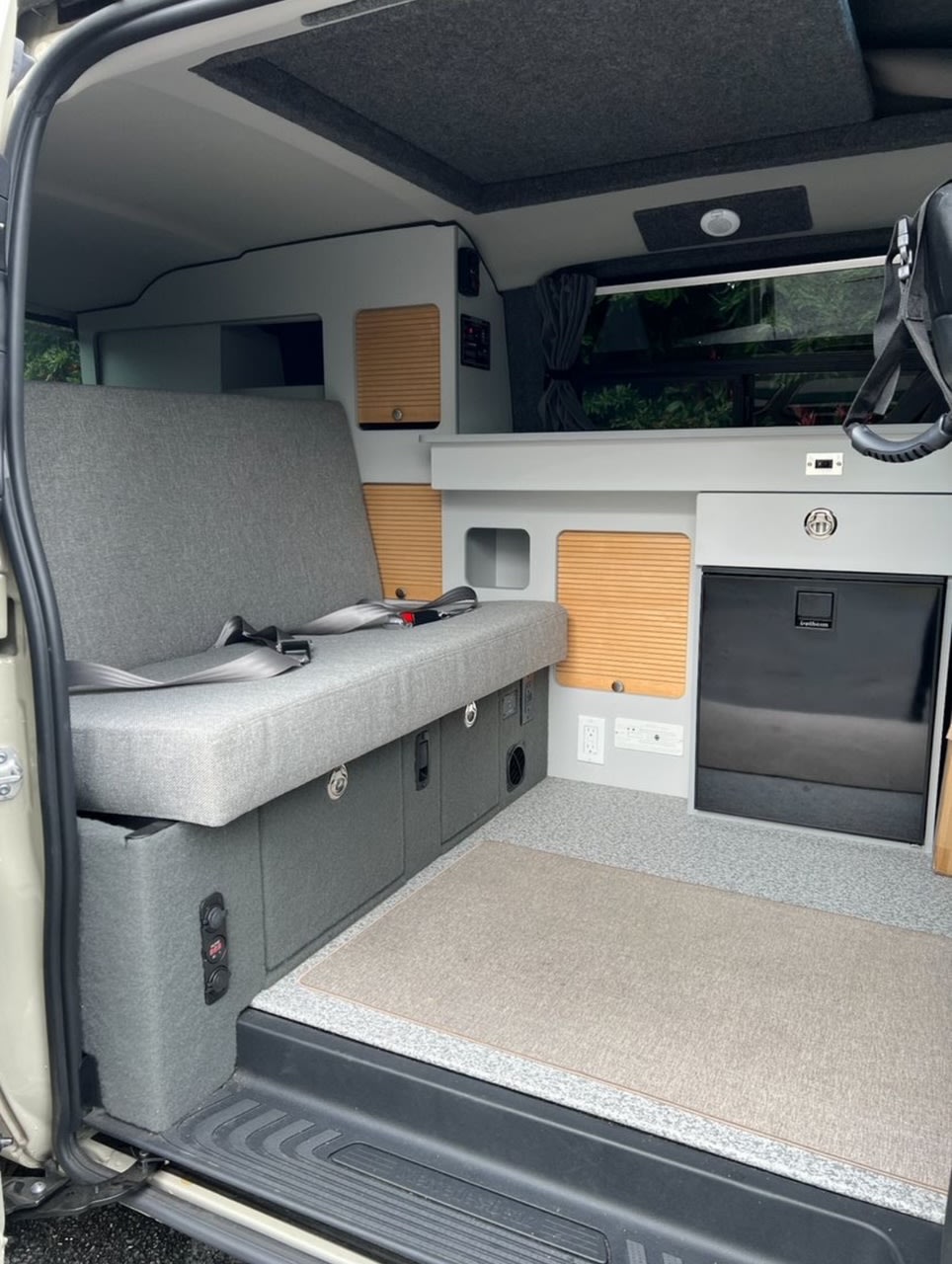 Interior of a functional RV rental. Shows a gray upholstered bench, wood-slat cabinets, fridge, and power outlets.. Mercedes-Benz Metris by GTRV 2019