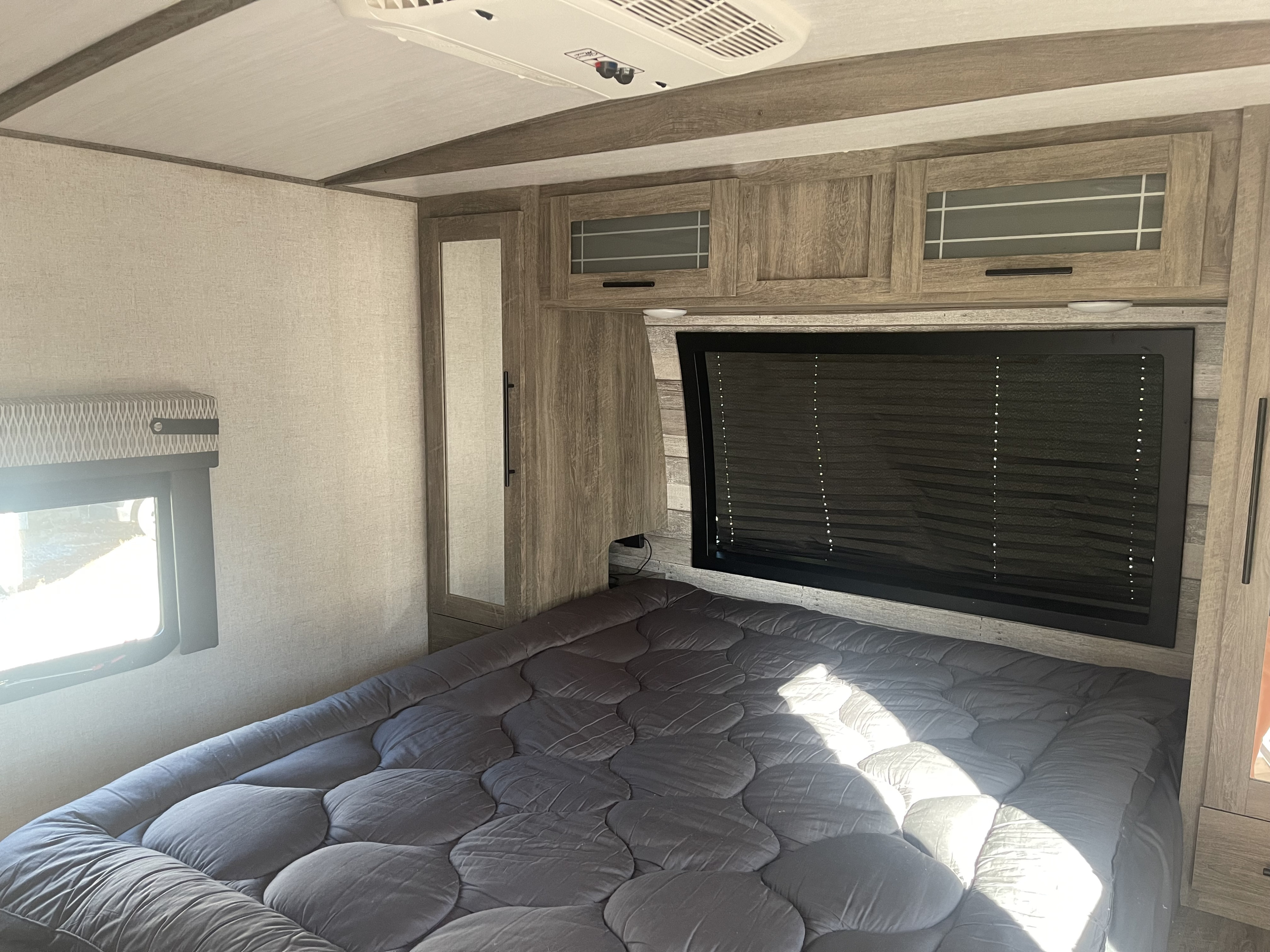 Cozy RV rental bedroom with a large bed, overhead cabinets, mirrored closet, and sunlit window for comfortable travel.. Forest River Salem Hemisphere 2020