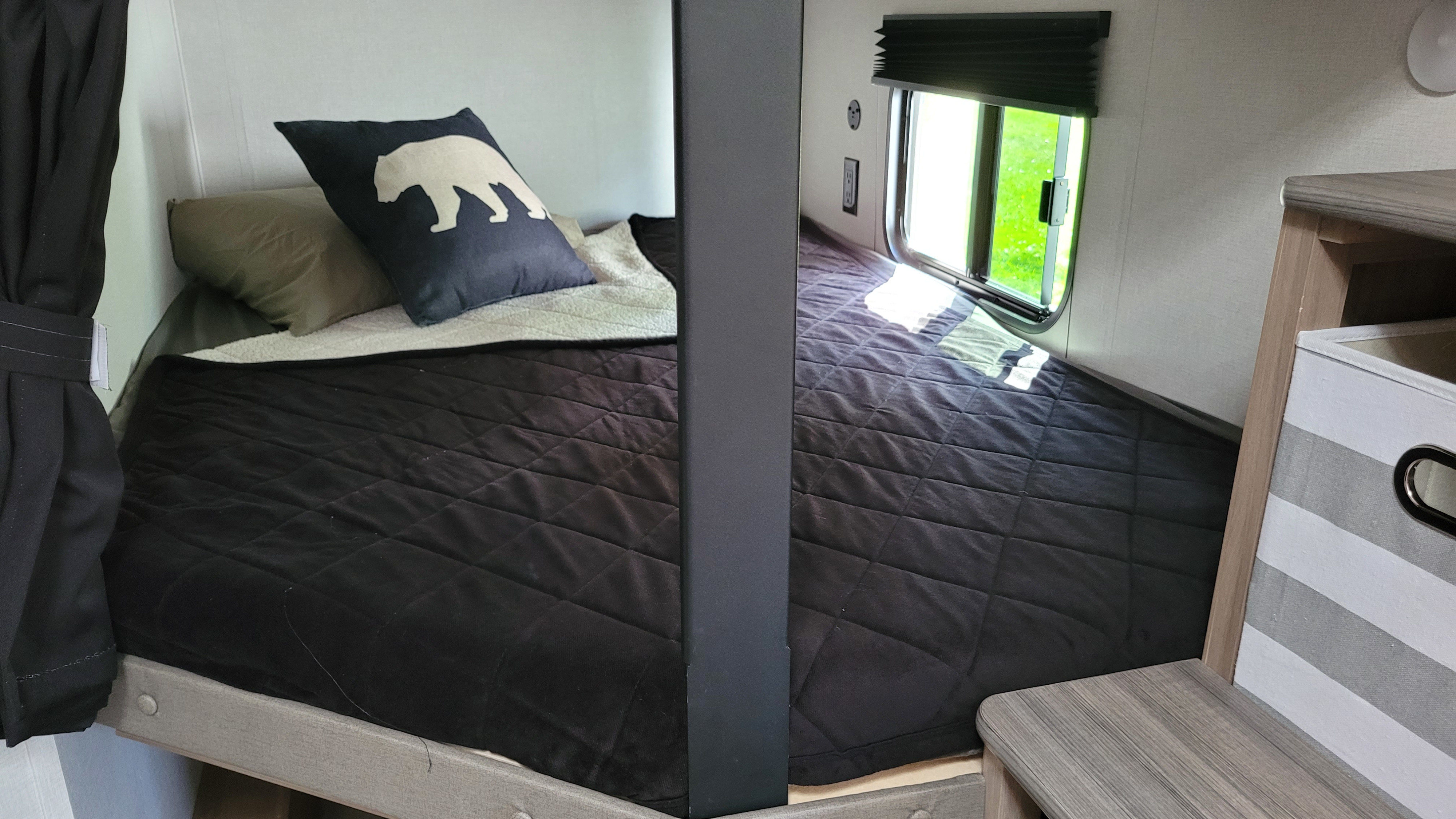 RV rental interior showing cozy bunk beds, a bear pillow, and a window overlooking greenery.. coleman Lantern 2025