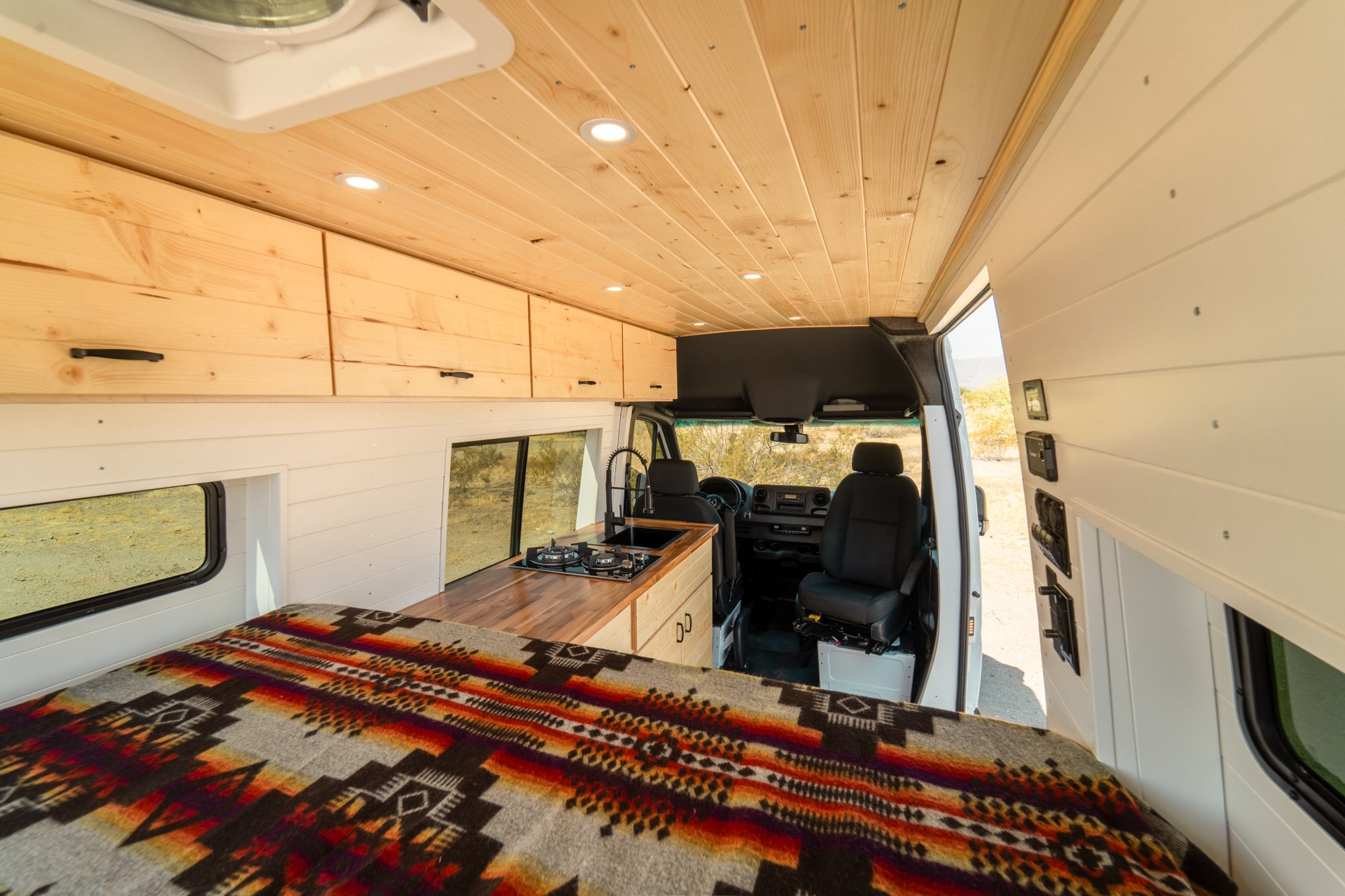 Bright and modern rv rental interior featuring custom wood ceilings, overhead cabinets, a cozy bed, and a full kitchen.. Mercedes-Benz Sprinter 2021
