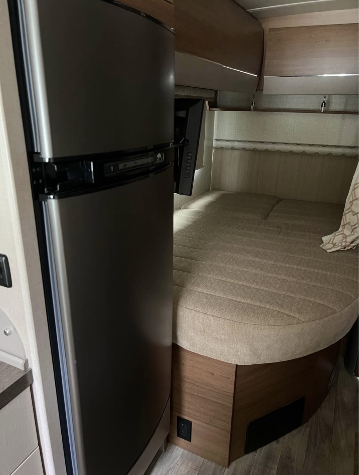 Inside an RV rental: a compact refrigerator, a wall-mounted TV, and a cozy bed area, ideal for travel.. Winnebago View 2017