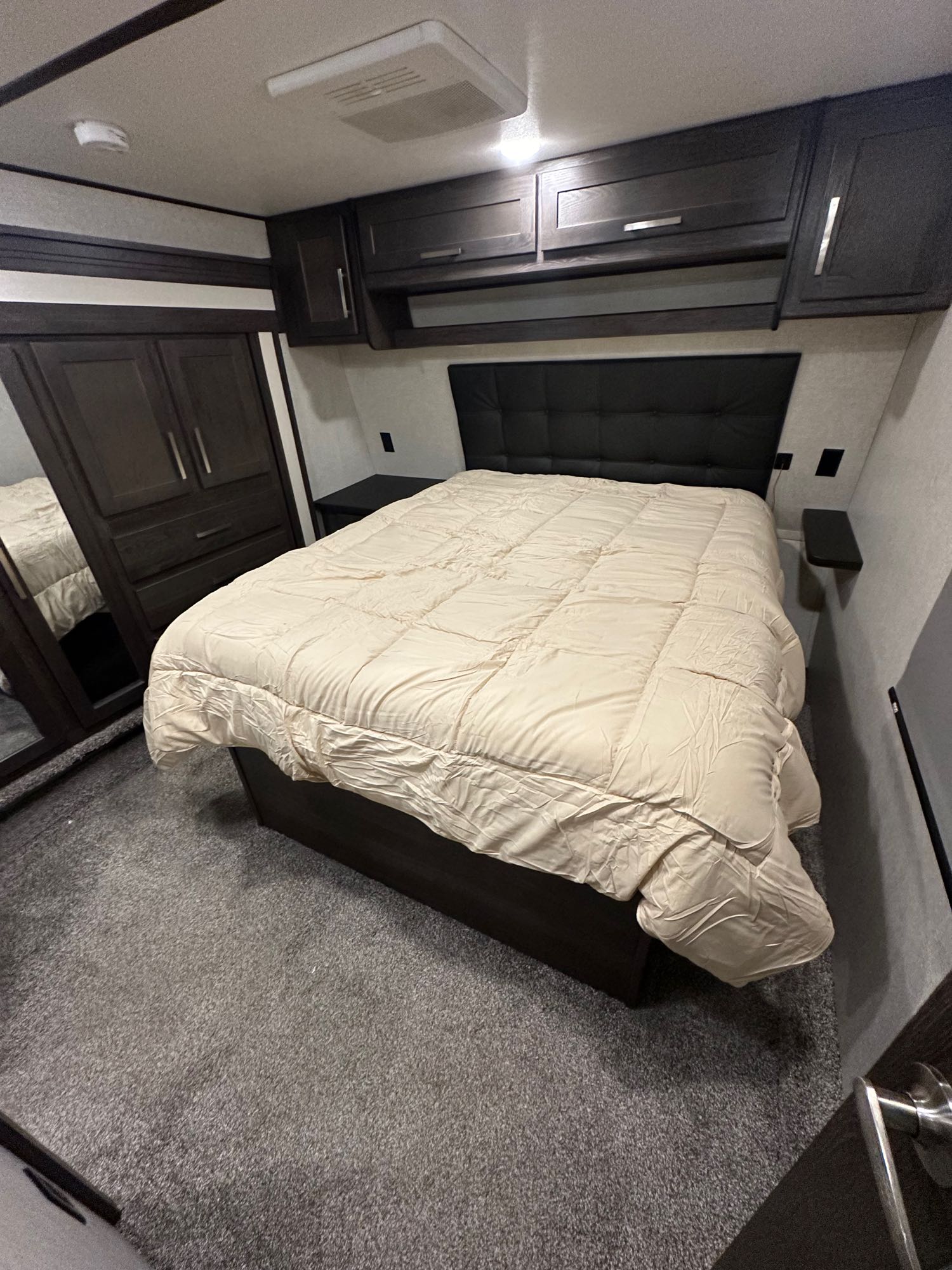 This spacious RV rental bedroom offers a large bed with a padded headboard, dark cabinetry, and grey carpet.. Keystone Raptor 2019