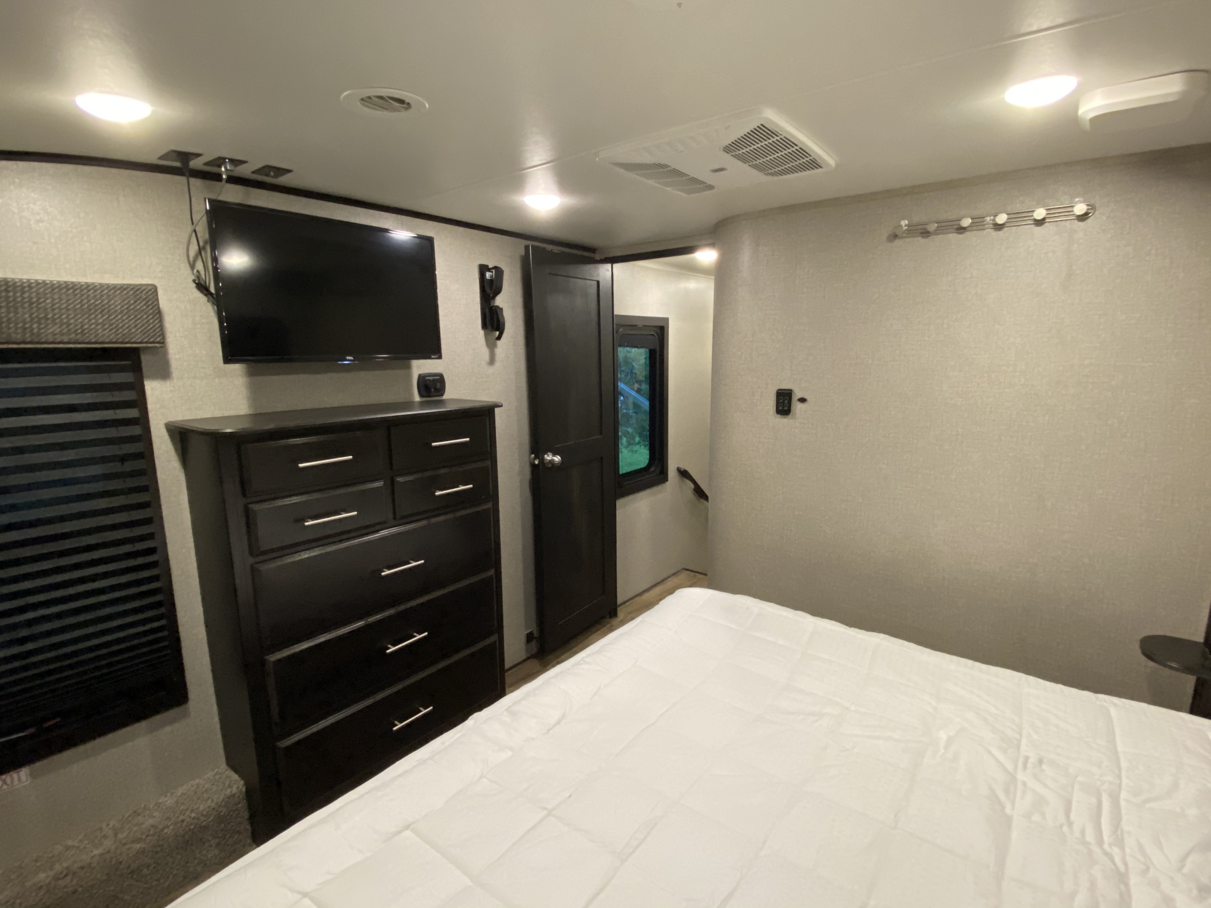 Modern RV rental bedroom with a comfortable bed, dresser, TV, and window, offering a cozy space for your journey.. Jayco Eagle 2020