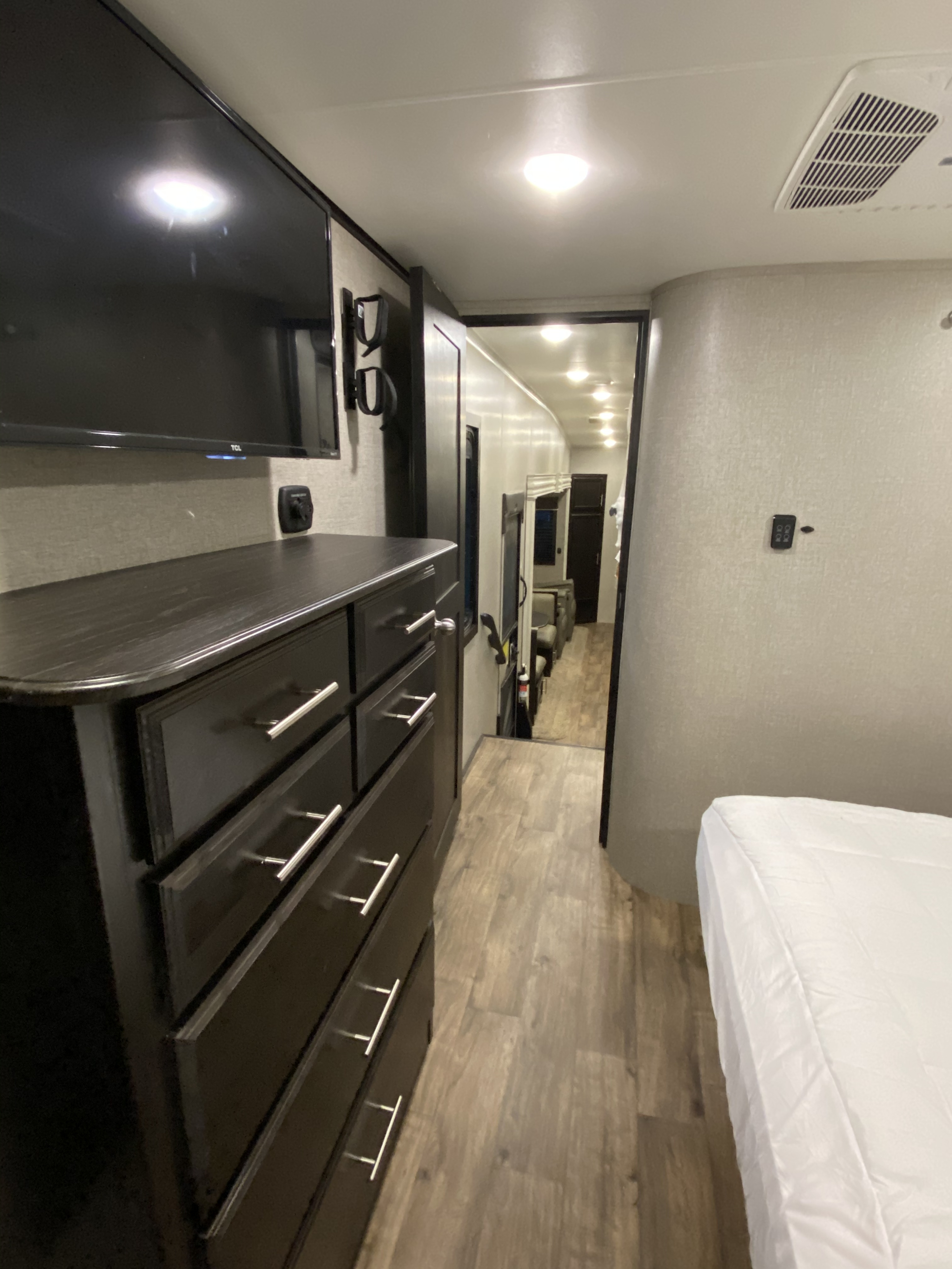 An RV rental's bedroom area with a dresser, TV, and an open hallway leading into the main living space. Clean and well-lit.. Jayco Eagle 2020