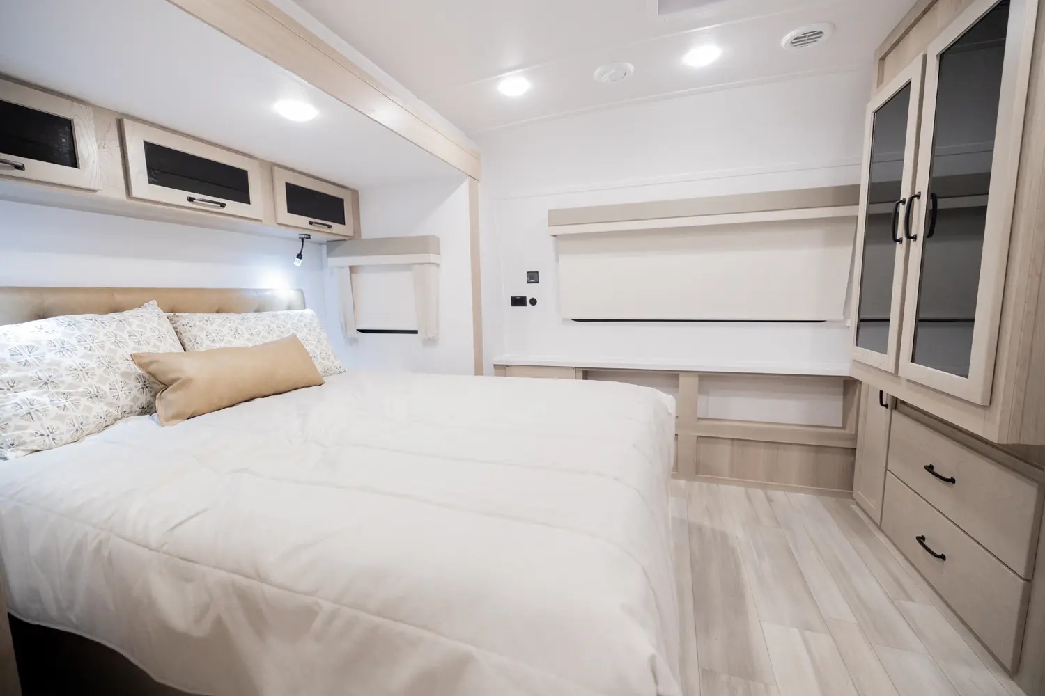A modern RV rental bedroom features a comfortable bed, light wood overhead cabinets, and window blinds, offering a cozy retreat.. Forest River Flagstaff Super Lite 2024