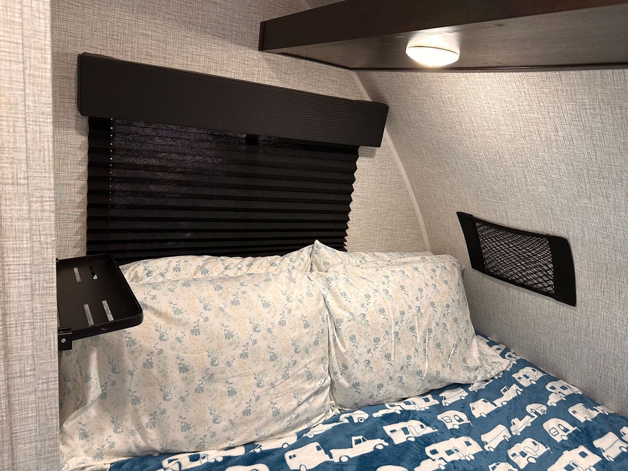 RV rental: cozy bedroom featuring bed with camper blanket, patterned pillows, window blinds, and storage net.. Braxton Creek FreeSolo DIN 2023