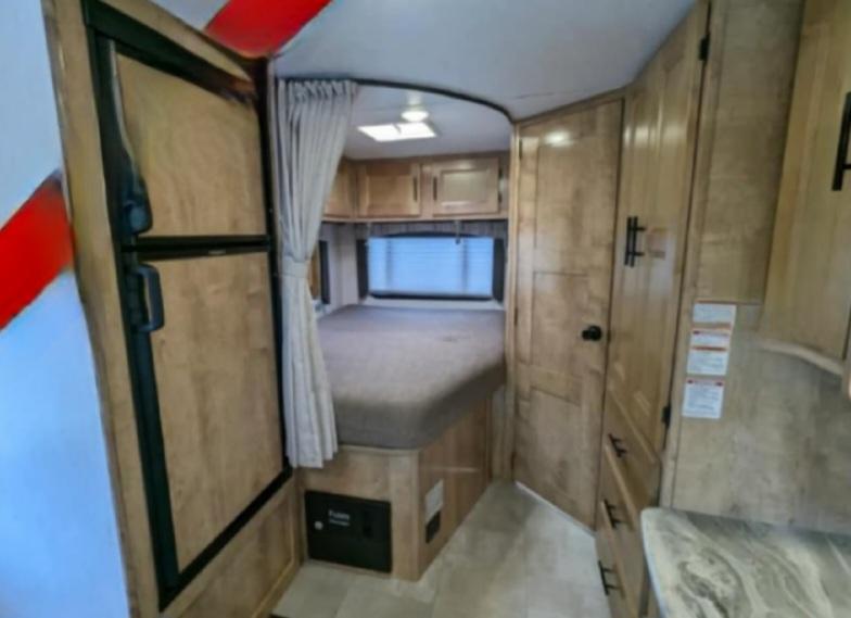 RV rental interior features a compact bedroom with a bed and window, plus a fridge and storage cabinets.. Ford coachman leprechaun 2021