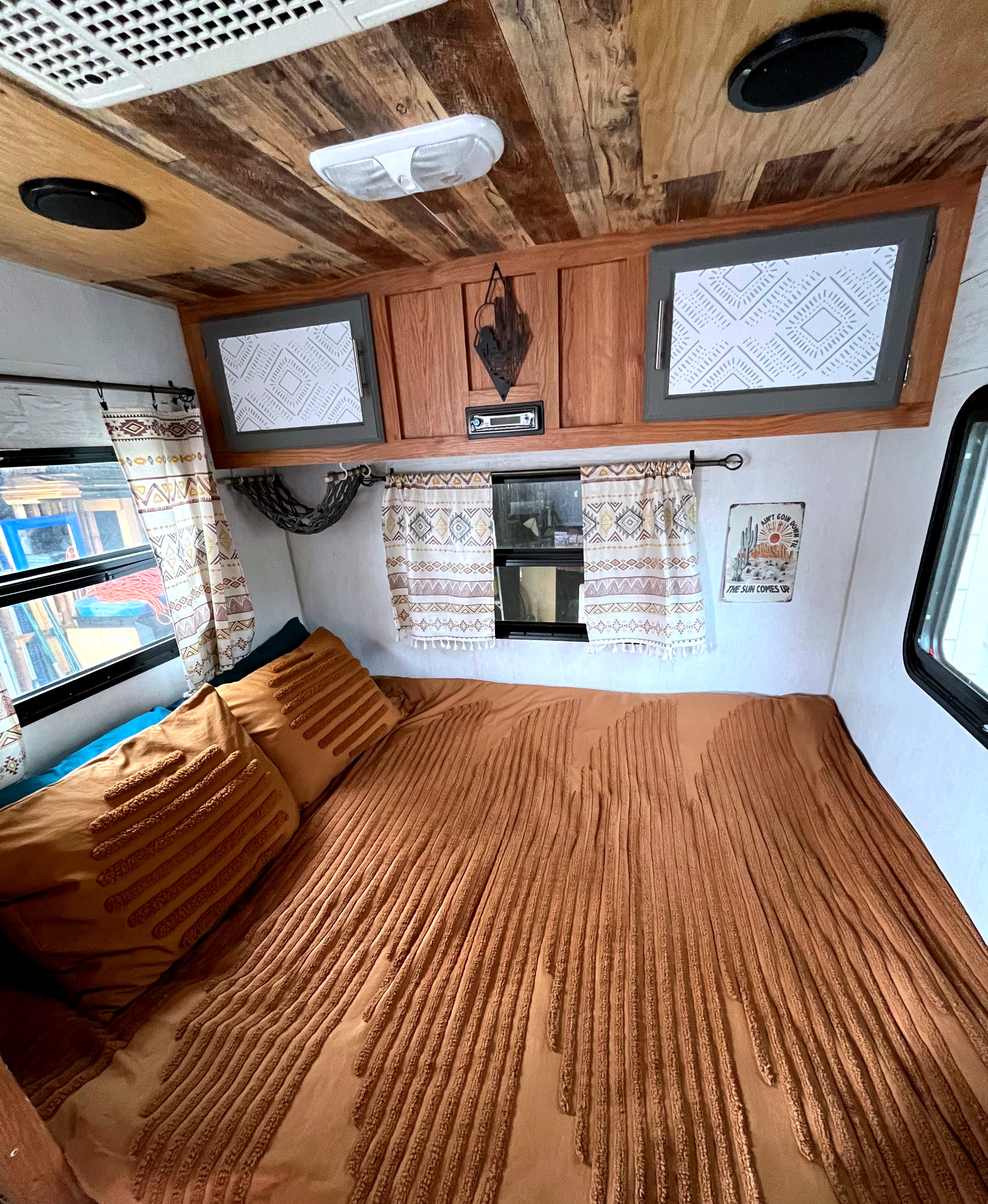 This cozy RV rental interior features a full bed with textured covers, patterned curtains, and custom wooden ceilings.. Sidekick 15F60 2008