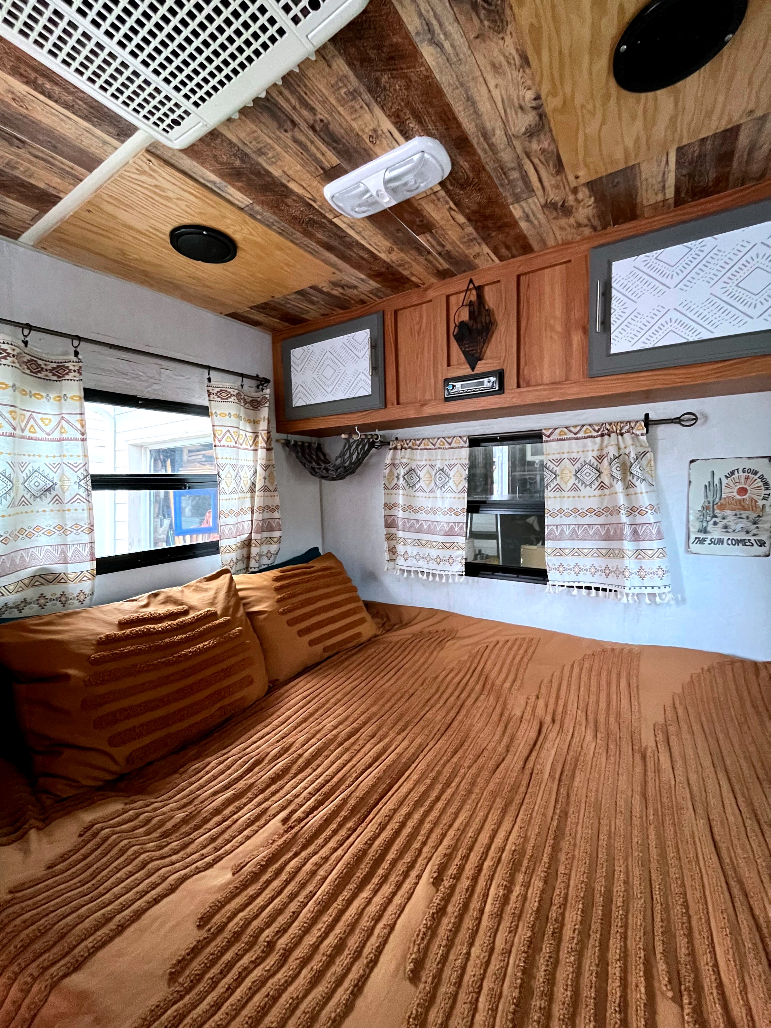 Warm & inviting RV rental bedroom with textured orange bedding, patterned curtains, and rustic wood ceiling.. Sidekick 15F60 2008