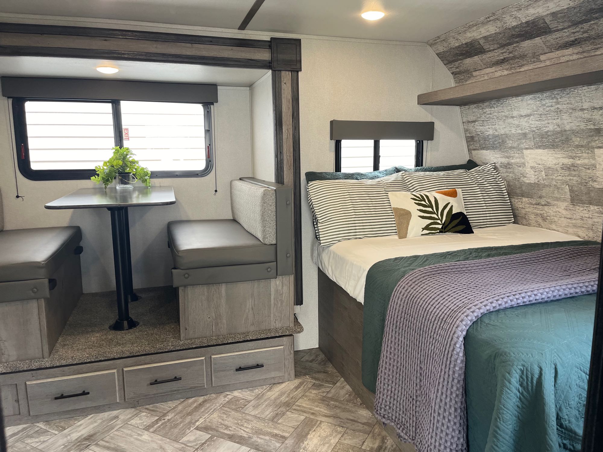 This RV rental interior features a cozy bed with striped pillows, a dinette booth, and ample storage.. Keystone RV Springdale 2021