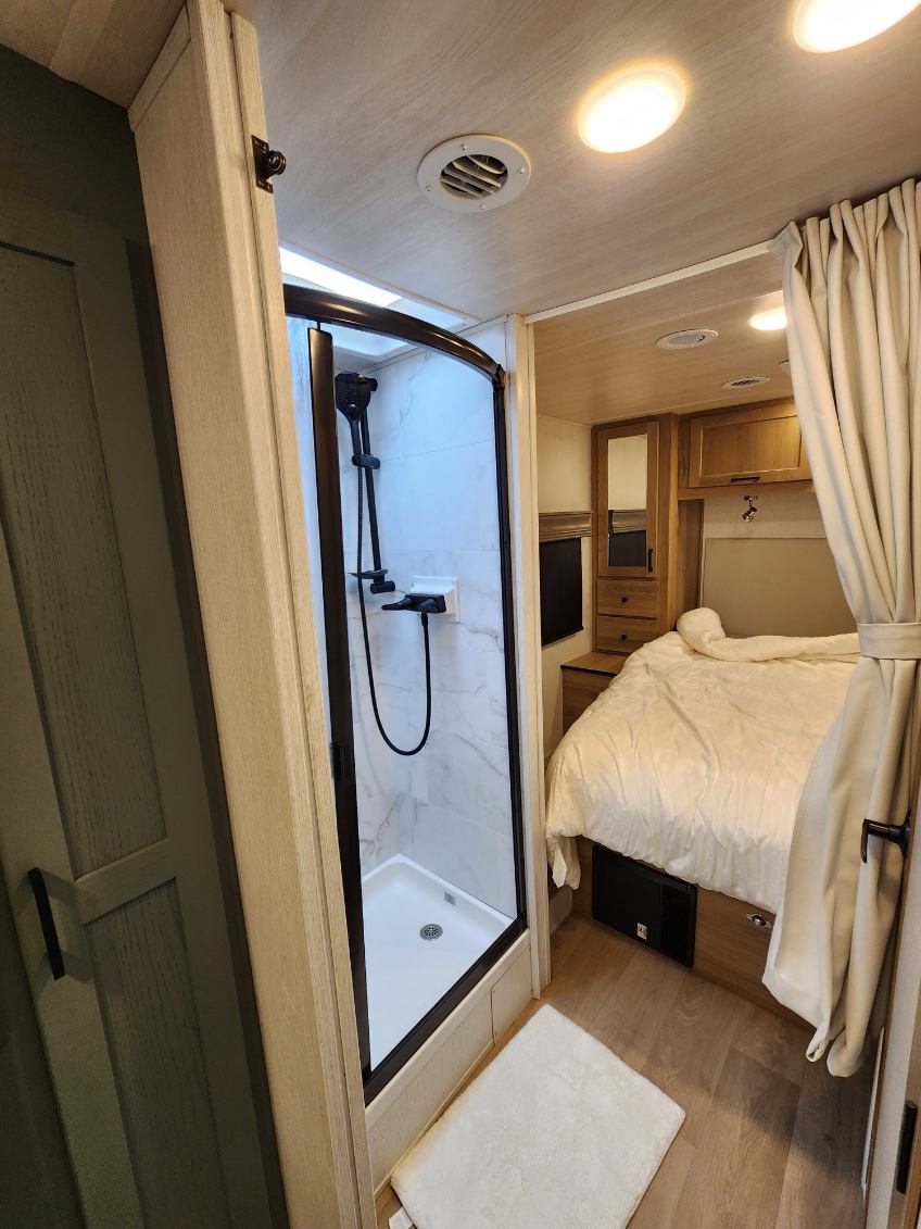 This RV rental shows a well-appointed interior with a compact shower stall and a comfortable bedroom area.. NeXus Triumph 31T 2024