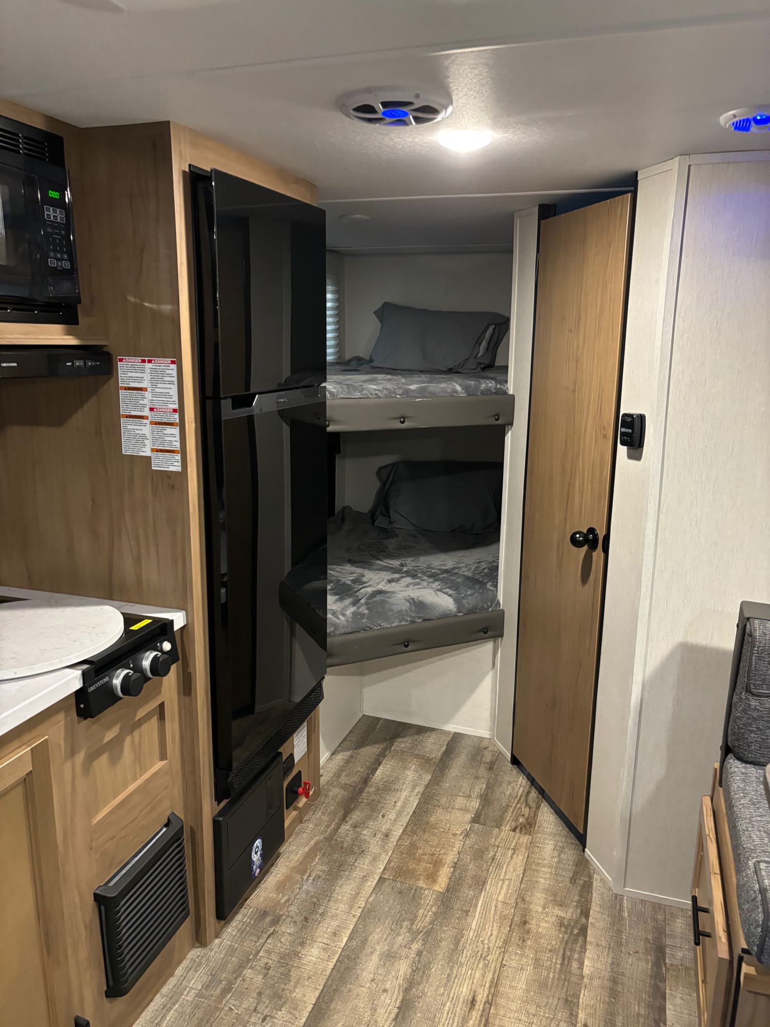 Compact RV rental interior featuring a kitchen area with a microwave, a refrigerator, and cozy bunk beds.. Forest River Cherokee Wolf Pup 2023