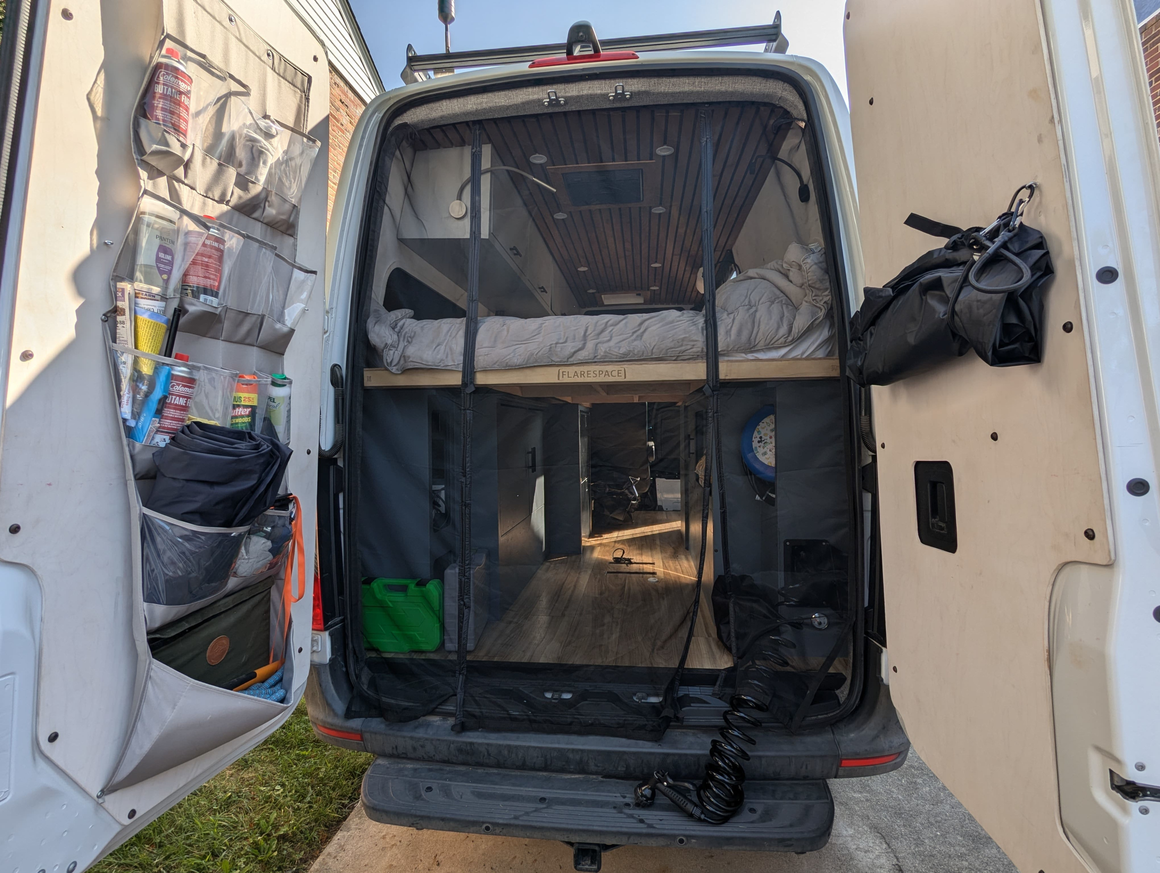 Inside a modern RV rental camper van from the rear, showing a raised bed, organized storage, and a protective mesh screen.. Mercedes-Benz sprinter 2020