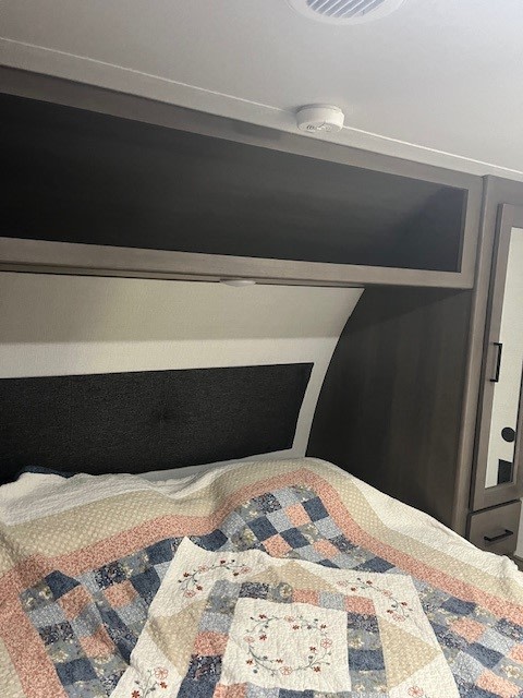 RV rental bedroom: patterned quilt, overhead storage, and ceiling smoke detector for travel safety.. Grand Design Transcend Xplor 2024