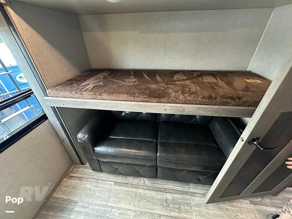 Inside this RV rental, a cozy bunk bed with a brown blanket is positioned above a black leather couch, optimizing space for rest.. Keystone RV Outback 2021