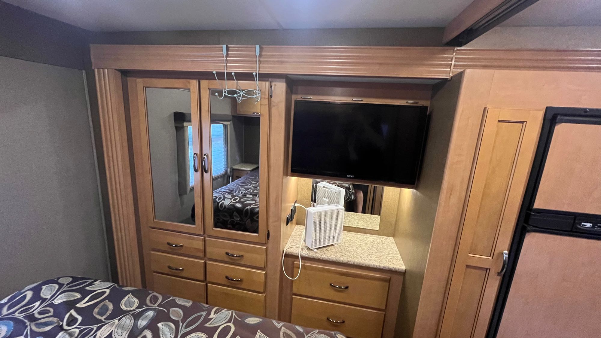 Spacious RV rental bedroom featuring mirrored wardrobe, many drawers, TV, and refrigerator, offering comfort and convenience.. Thor A.C.E. 2016